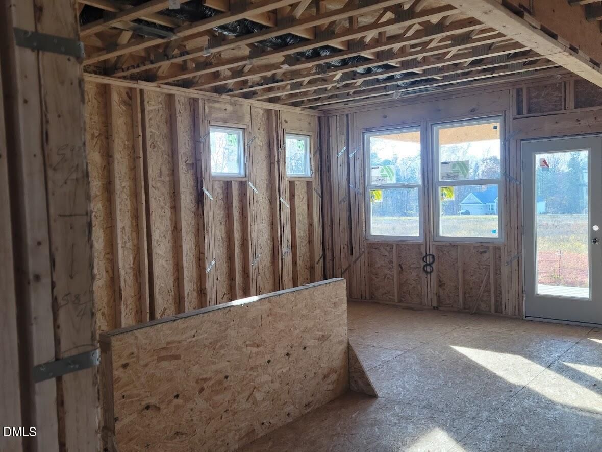 Unfinished living space with exposed wooden beams, plywood walls, and large windows in The Willow G 5-bedroom home, Angier, NC