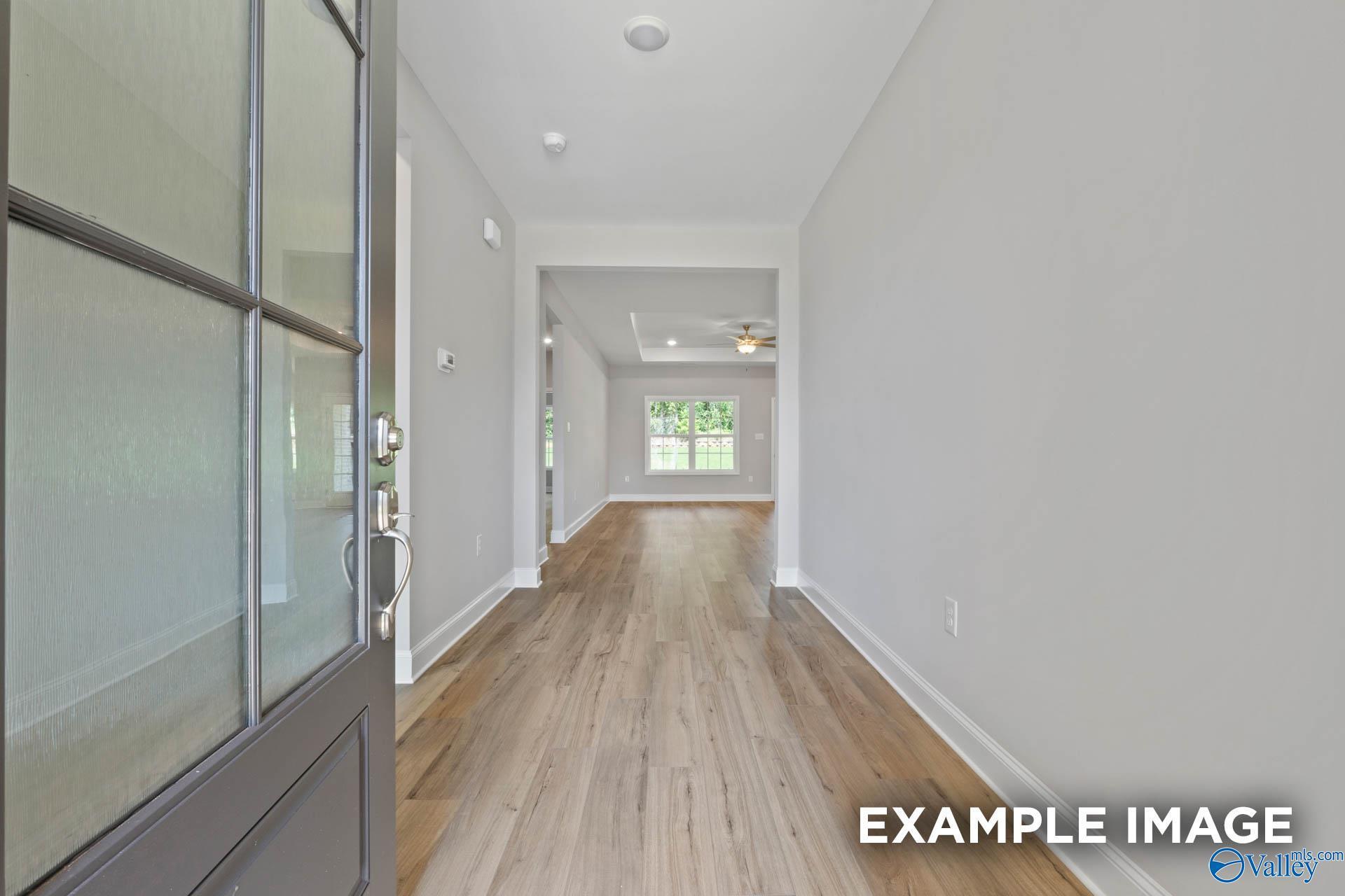 Welcoming entry hallway with hardwood floors, glass front door, and natural light in The Montgomery 3-bedroom home, Meridianville, Alabama