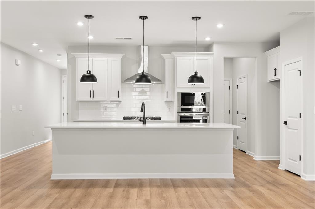 Modern white kitchen with large island sink, stainless steel appliances, and pendant lights in Davidson Homes The Cary A, Winder, GA