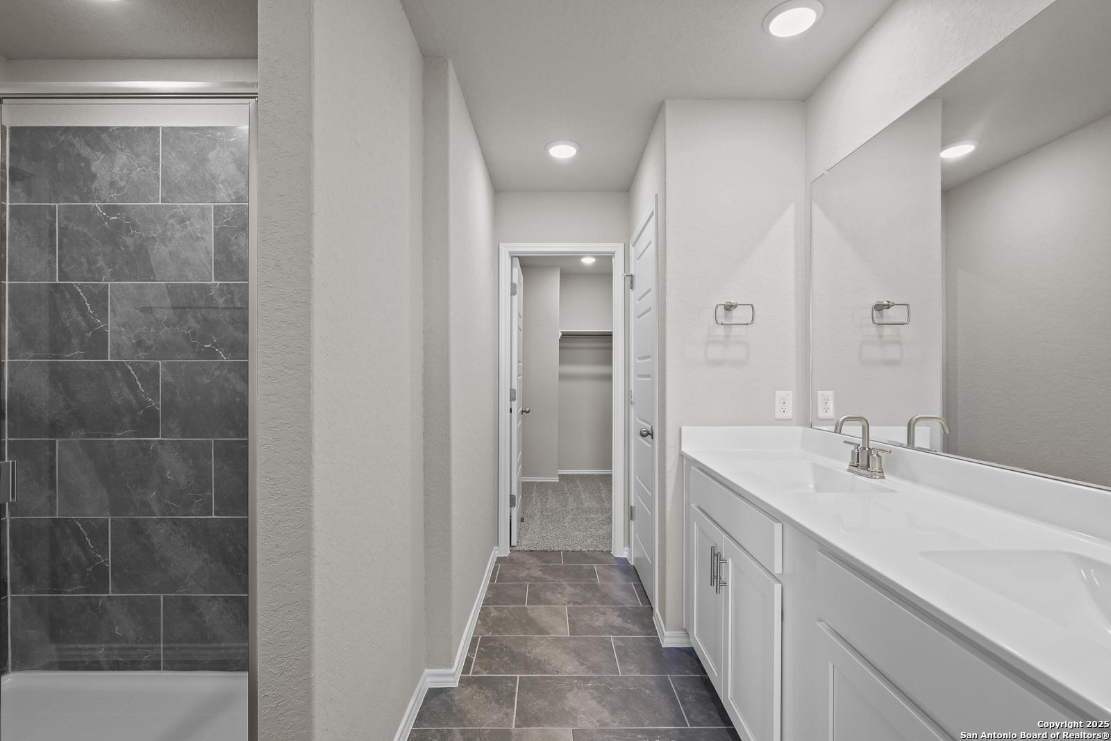 Modern master bathroom with slate-tile walk-in shower, double white vanity, mirrors, and closet access in Davidson Homes The Trinity D, San Antonio