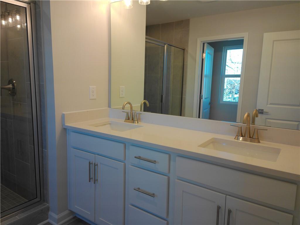 Modern master bath with white double vanity, gold faucets, large mirror, and glass shower in Davidson Homes The Marion C, Winder, GA