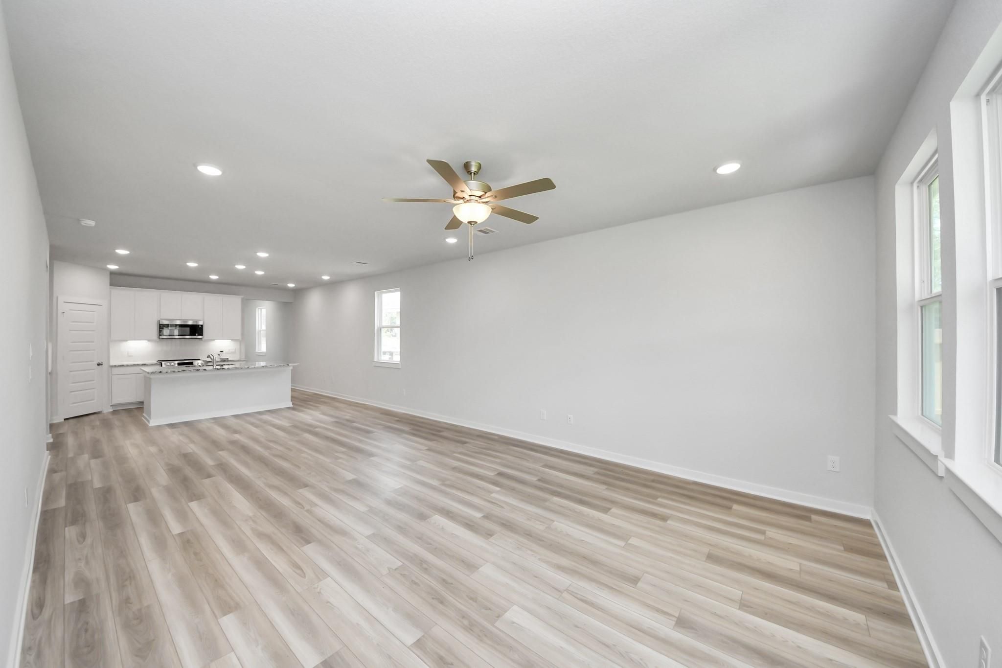 Open-concept living room with wood-look flooring and ceiling fan in The Sabine F floor plan at Liberty Estates, Texas.