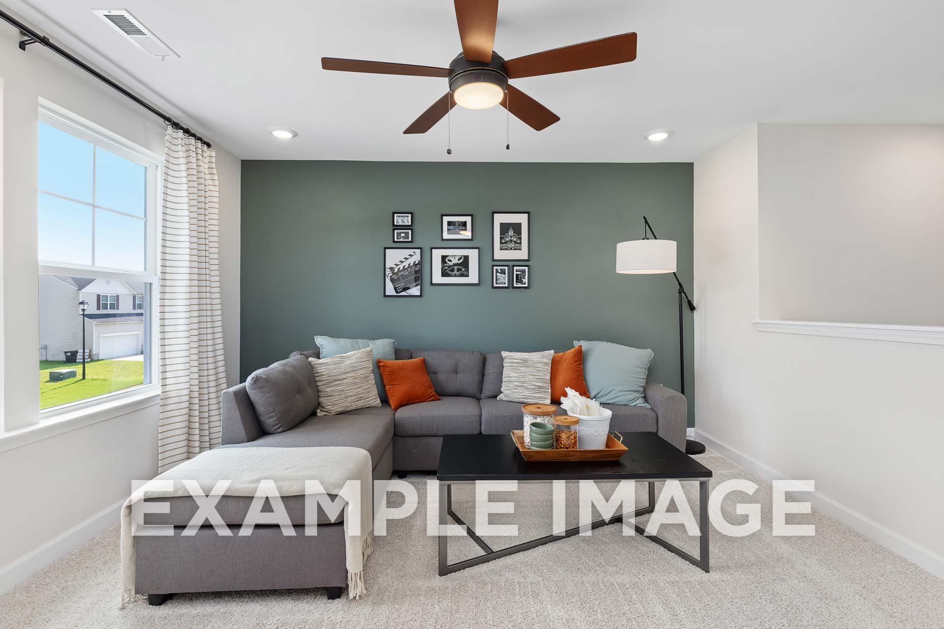 Cozy living room in The Willow E with gray L-shaped sectional, orange pillows, sage green accent wall, and large window