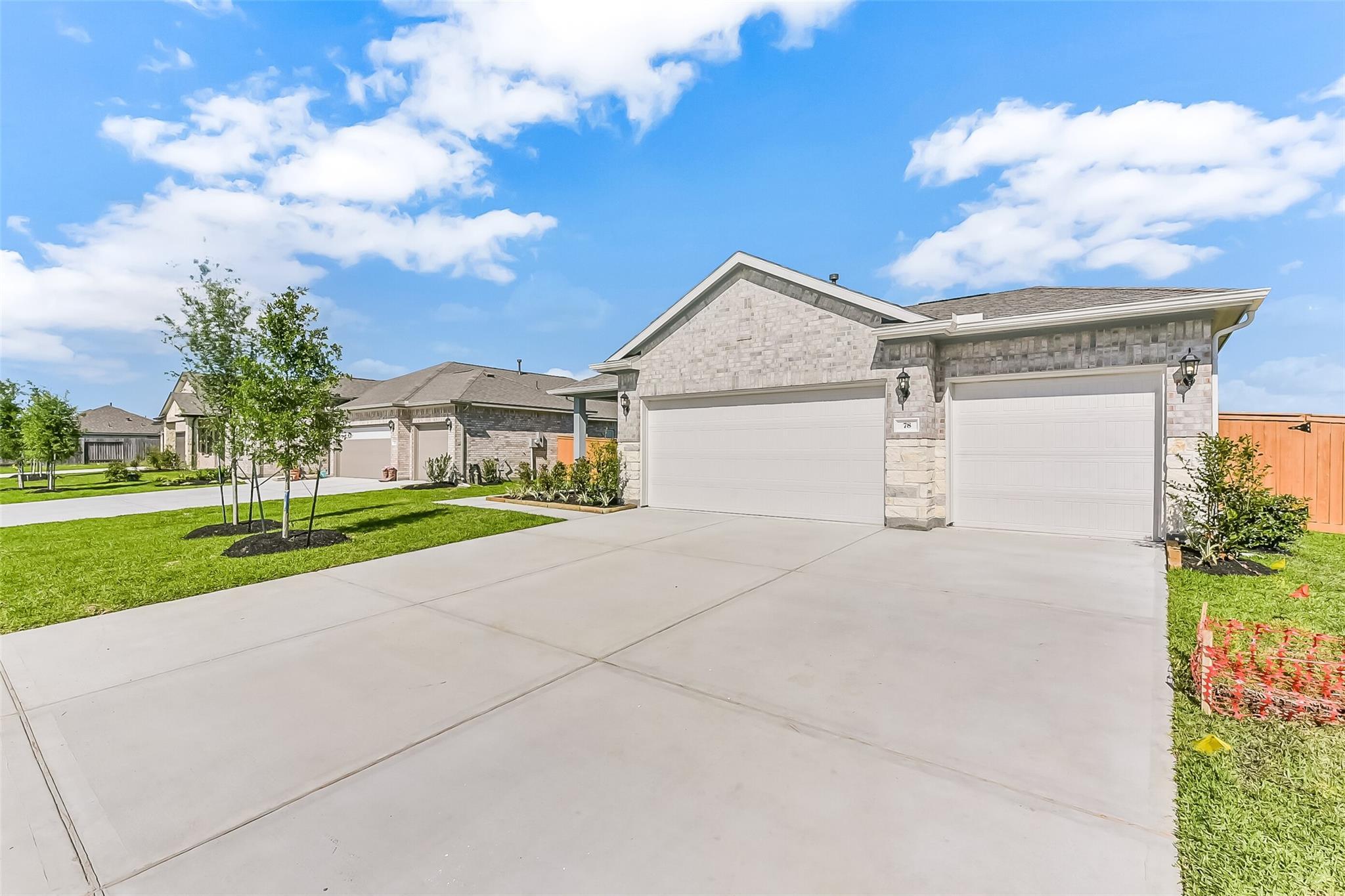 Modern brick single-story home with 3-car garage, driveway, and lush yard in River Ranch Meadows, Dayton, Texas by Davidson Homes