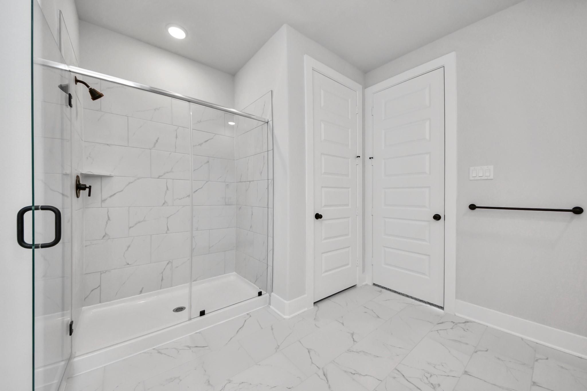 Modern walk-in shower with marble-look tile in The Laguna C floor plan by Davidson Homes in Sunterra, Katy, Texas.