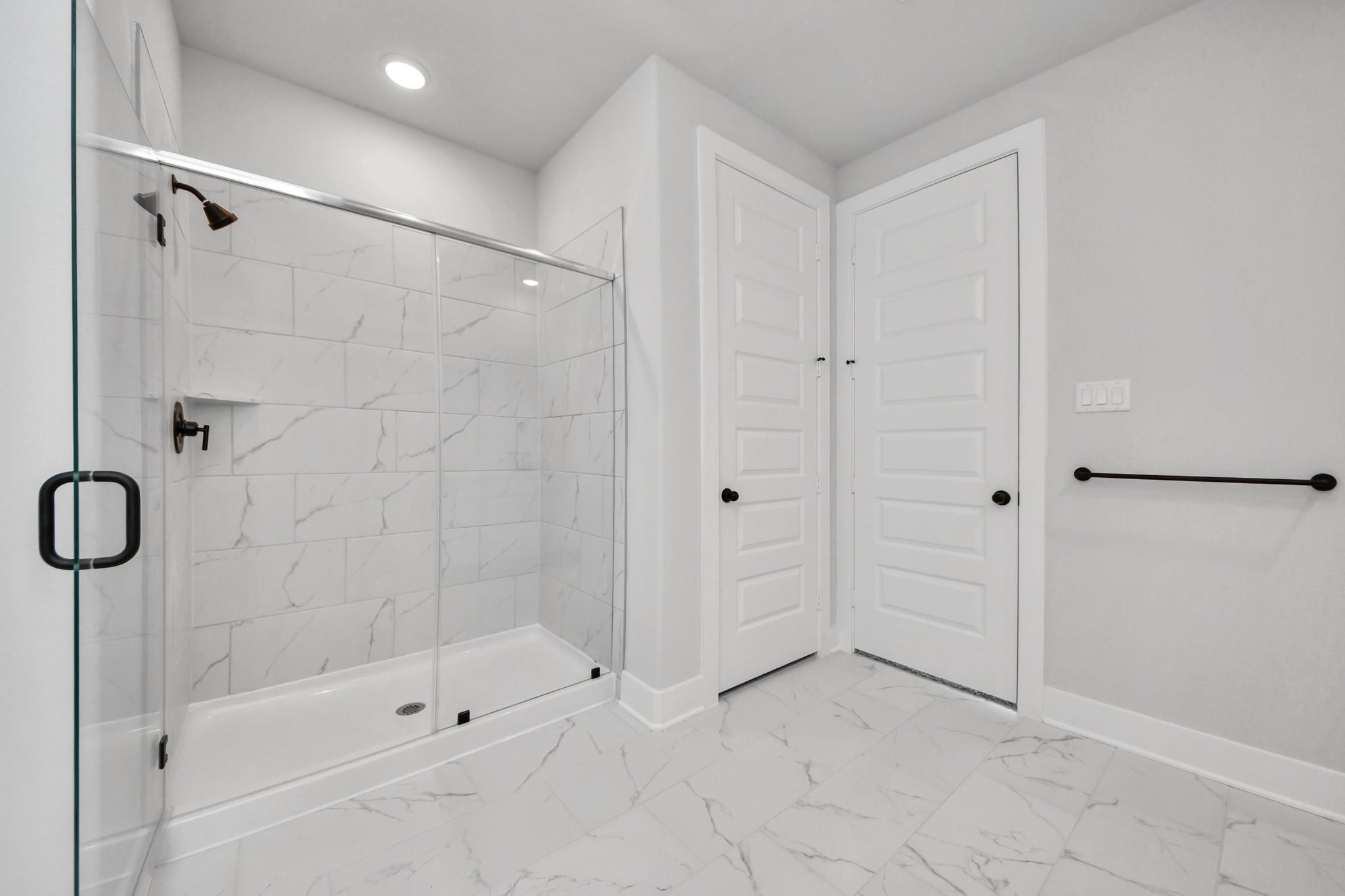 Modern walk-in shower with marble-look tile in The Laguna C floor plan by Davidson Homes in Sunterra, Katy, Texas.