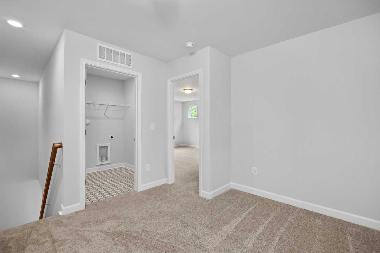 Upper floor laundry room in The Durham with open white door, tiled floor, utility sink, beige carpet hallway, Davidson Homes design