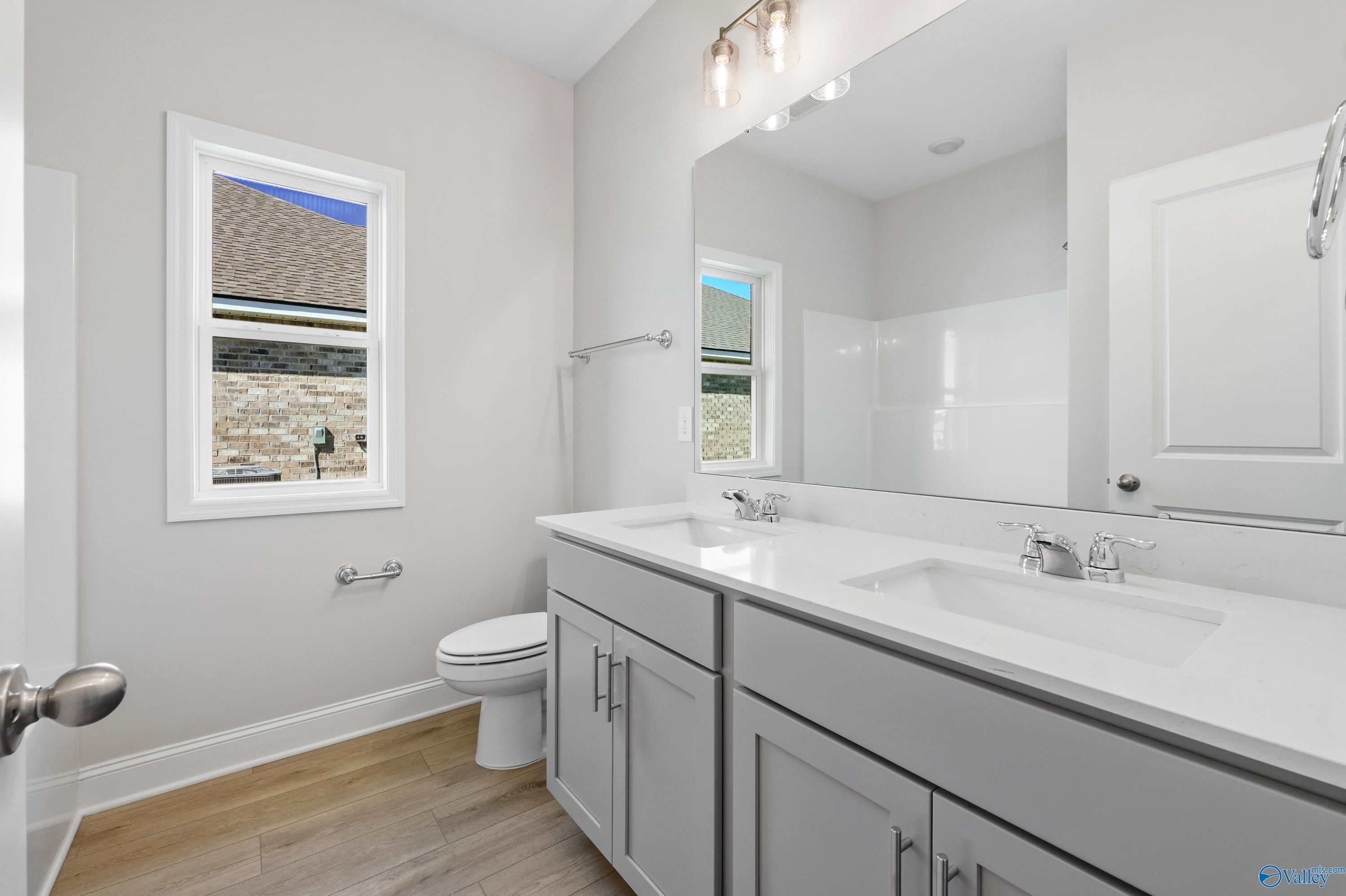 Modern master bathroom featuring double vanity with gray cabinets, large mirror, and window in Davidson Homes The Everett, Hazel Green, Alabama