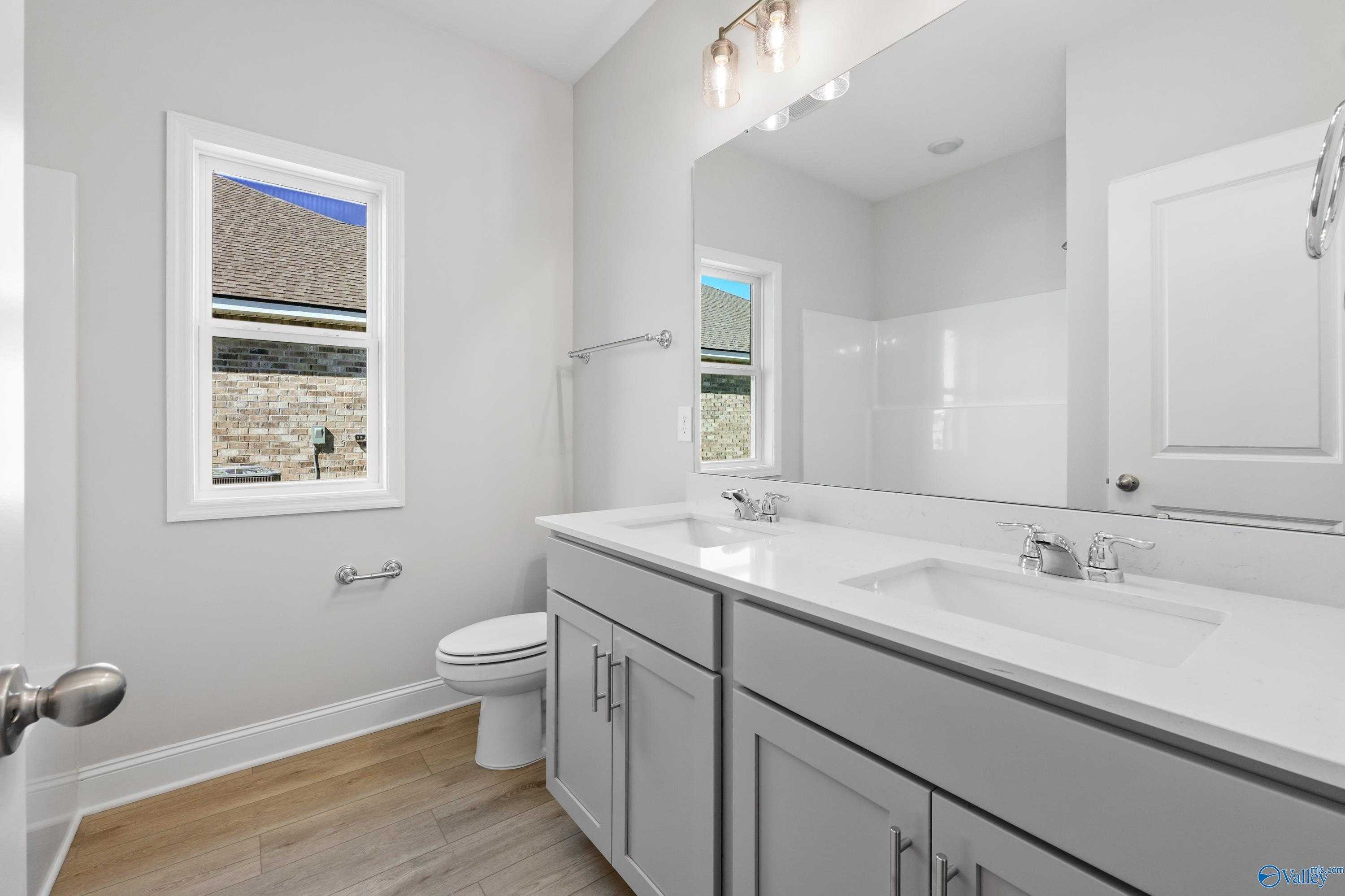 Modern master bathroom featuring double vanity with gray cabinets, large mirror, and window in Davidson Homes The Everett, Hazel Green, Alabama