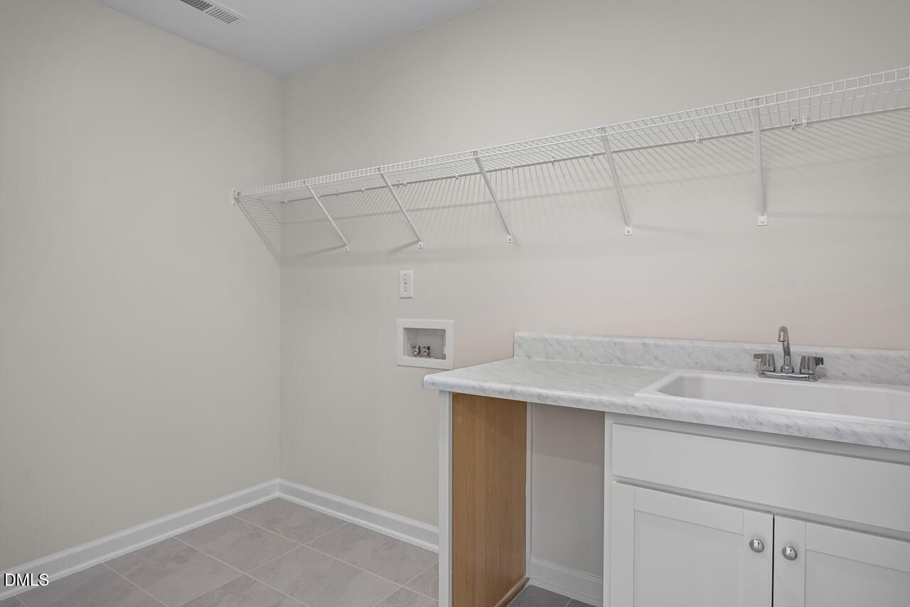 Laundry room with utility sink, white cabinets, and wire shelving in The Willow B floor plan, Woodland Crossing, Zebulon.