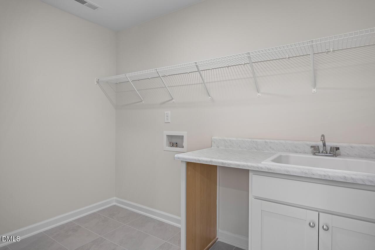 Laundry room with utility sink, white cabinets, and wire shelving in The Willow B floor plan, Woodland Crossing, Zebulon.