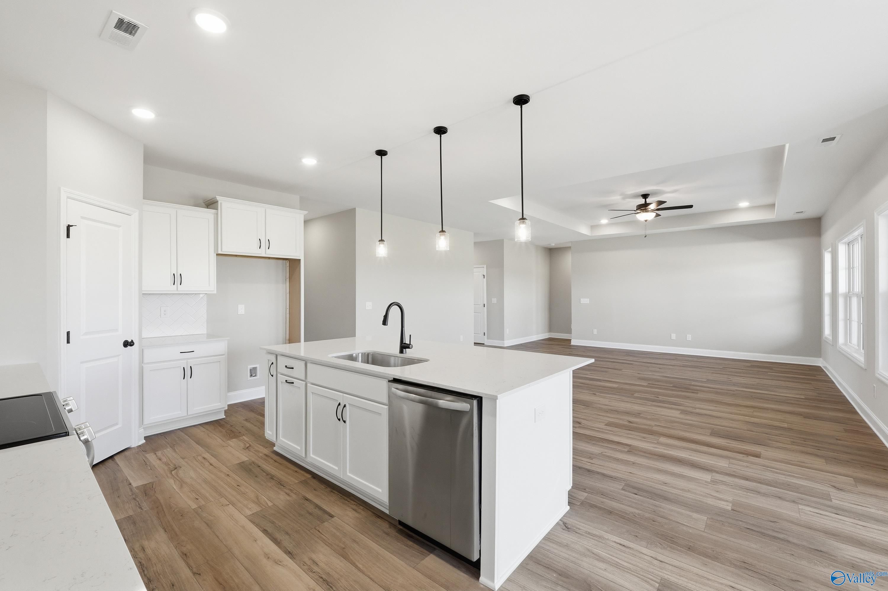 Modern open-concept kitchen with white island sink, stainless dishwasher, hardwood floors in Davidson Homes The Rockford, Harvest AL