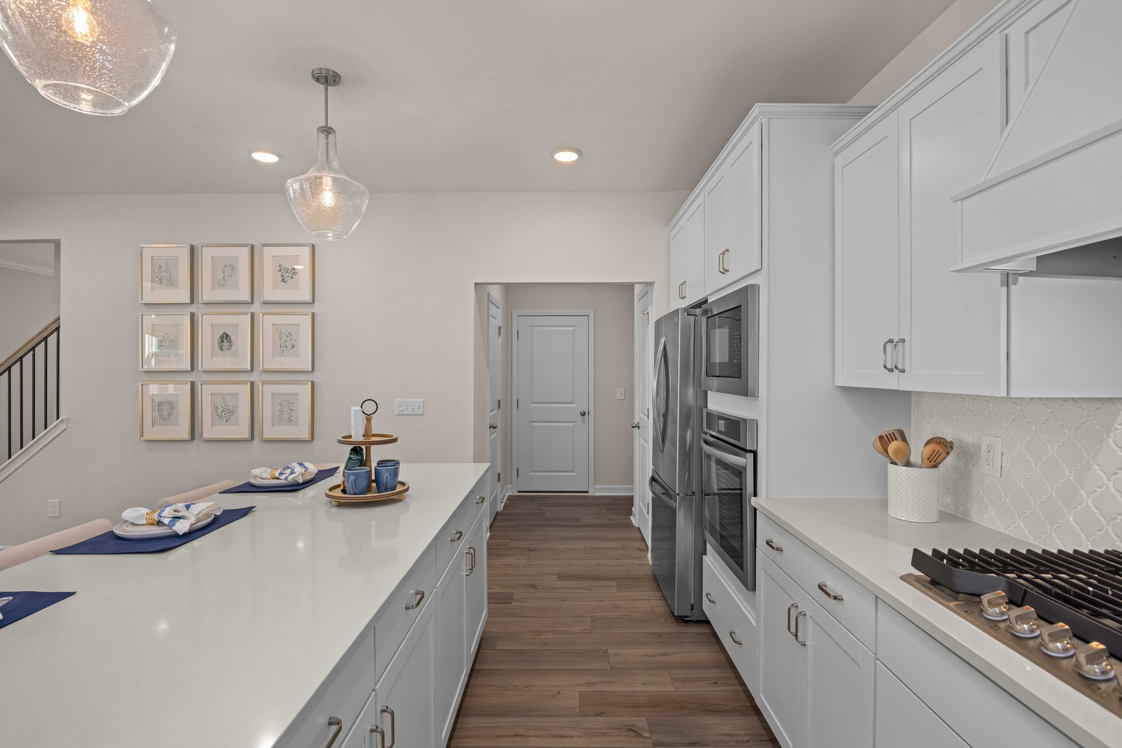 Modern white kitchen at Sage on North Main in Wake Forest NC with quartz island, stainless appliances, pendant lights, subway tile