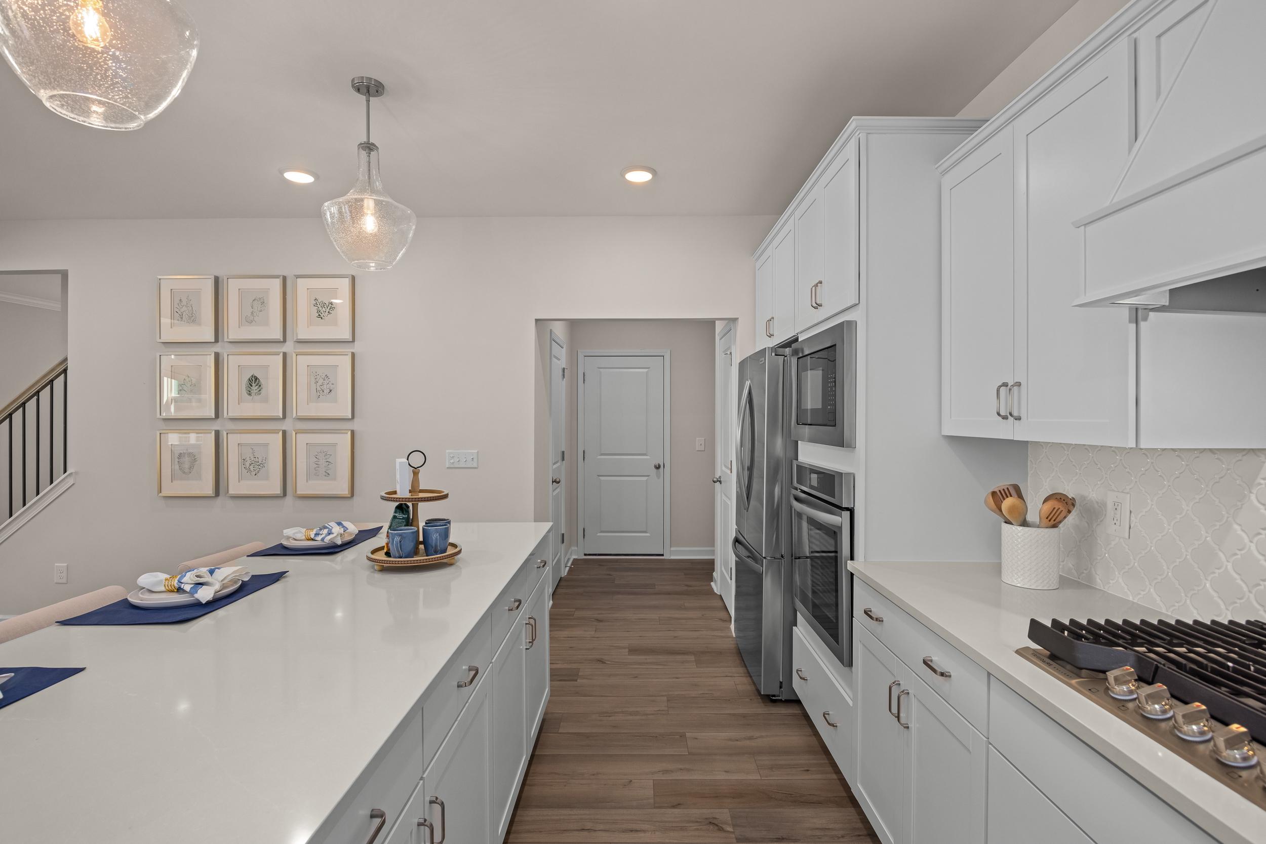 Spacious gourmet kitchen in The Hickory II with white shaker cabinets, quartz island, stainless appliances, subway tile backsplash