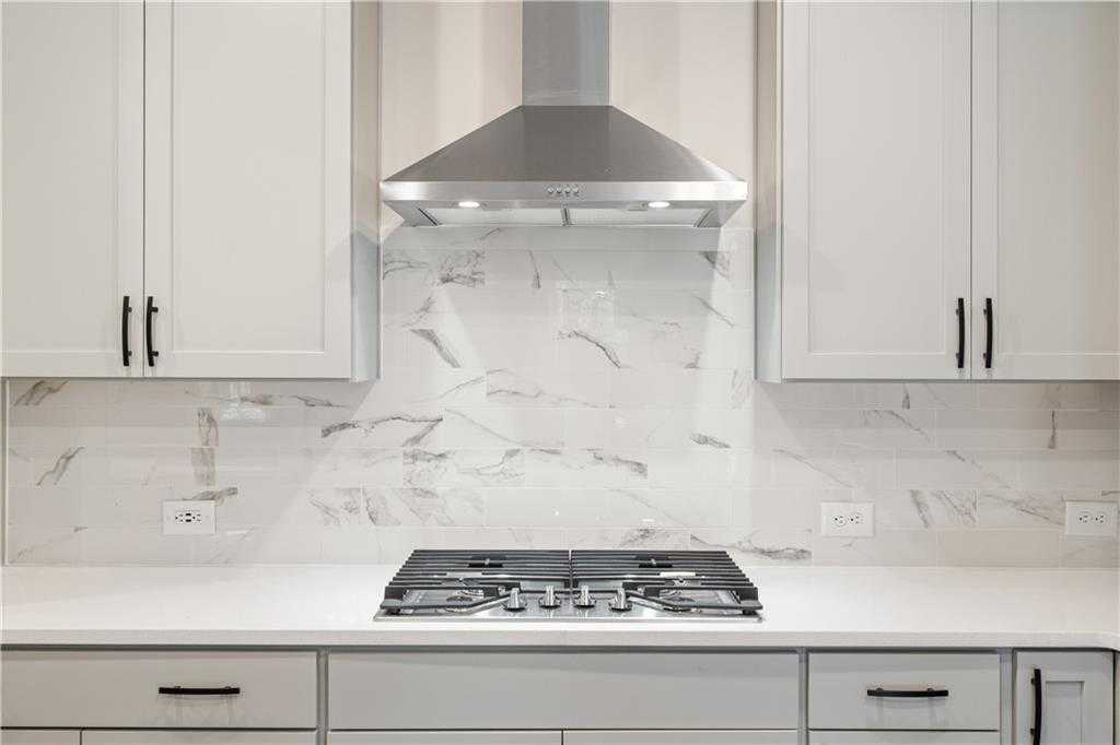 Modern kitchen featuring white shaker cabinets, stainless steel range hood, gas cooktop, and marble backsplash in The Daphne B, Loganville, GA