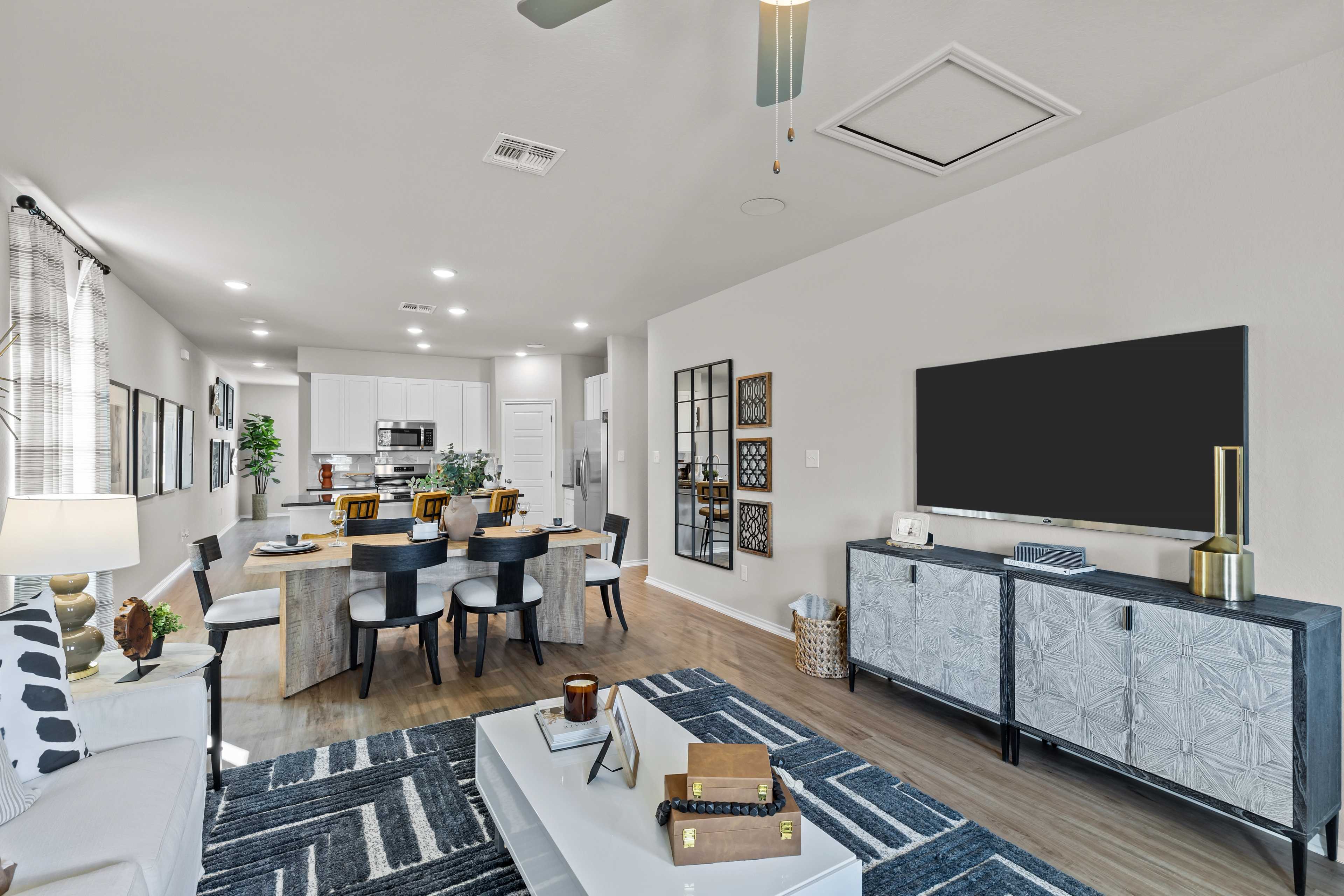 Spacious open-concept living room and kitchen in The Sabine C with modern white island, dining table, TV wall, and neutral decor
