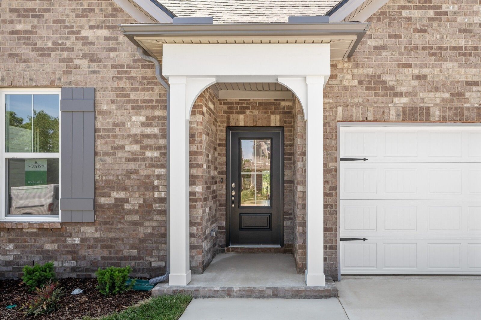 Brick front porch with arched entry, black front door, and 2-car garage at The Cottonwood E by Davidson Homes in Gallatin, TN