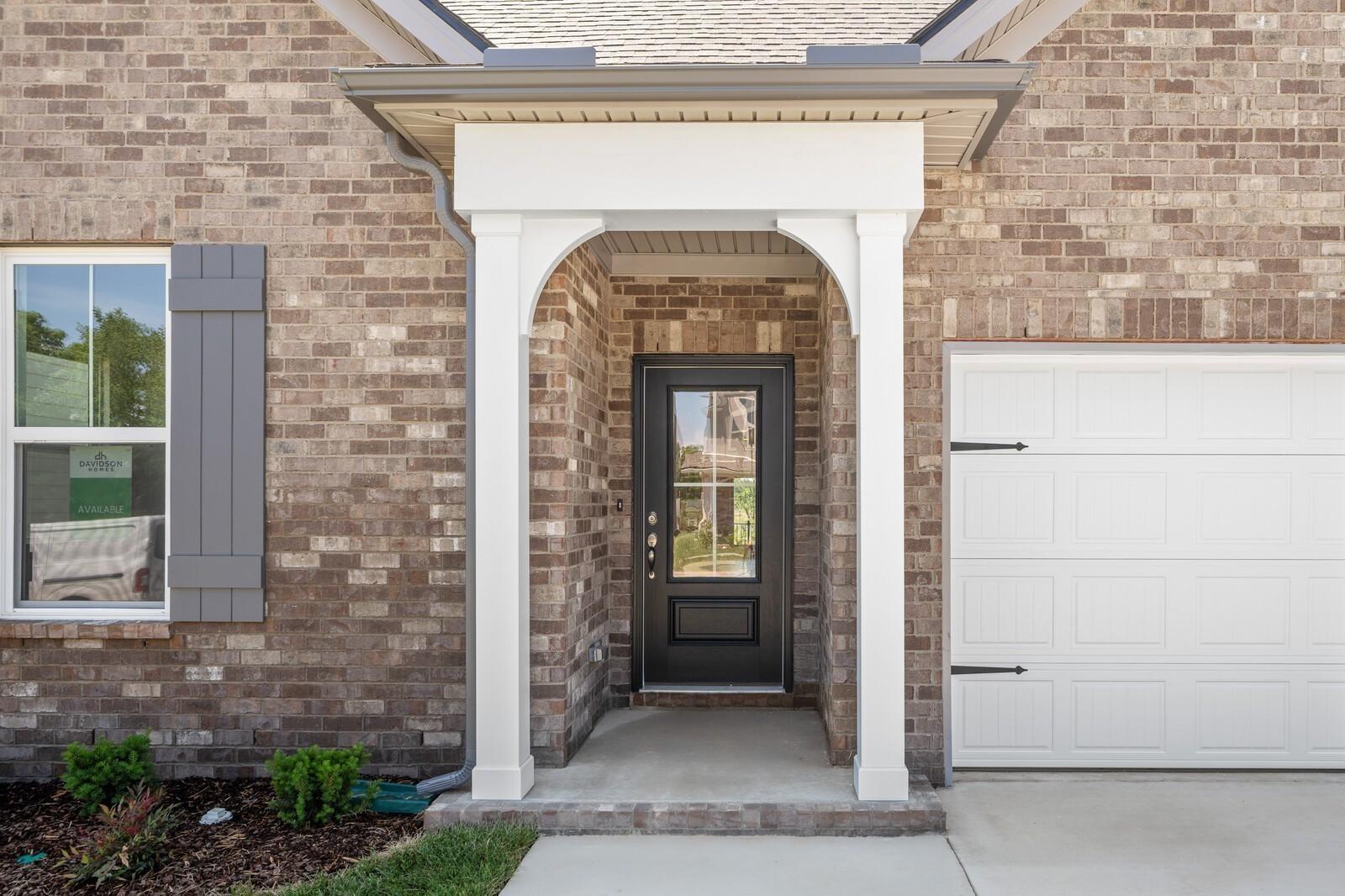 Brick front porch with arched entry, black front door, and 2-car garage at The Cottonwood E by Davidson Homes in Gallatin, TN