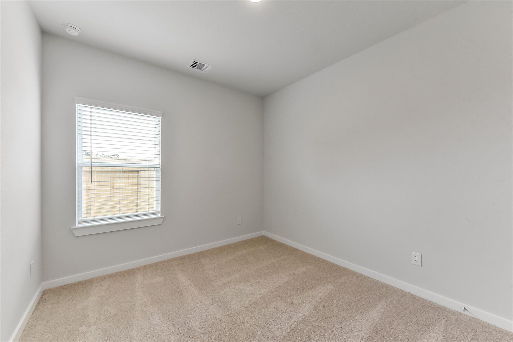 Spacious empty bedroom with light gray walls, beige carpet, window blinds in Davidson Homes The Sabine F, Dayton, Texas