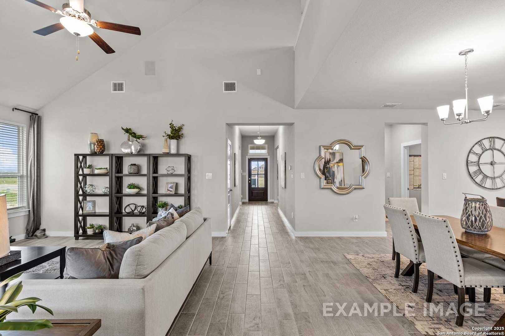 Open living room with white sofa, wooden dining table, bookshelf, and hallway in Davidson Homes Collin B, Hannah Heights, Seguin, Texas