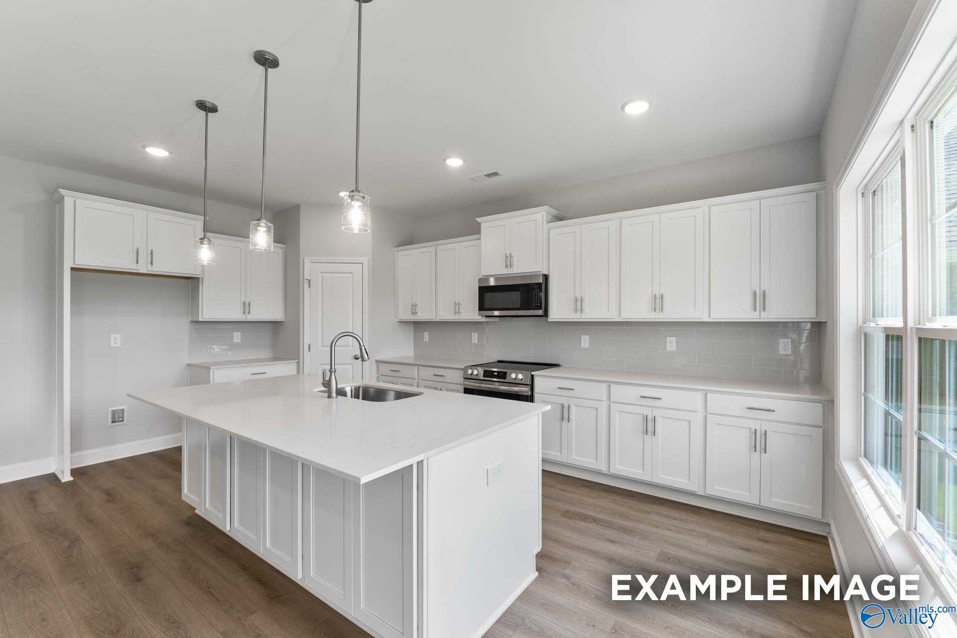 Modern white kitchen with island sink, stainless appliances, and pendant lights in Davidson Homes The Madison A, Harvest, Alabama