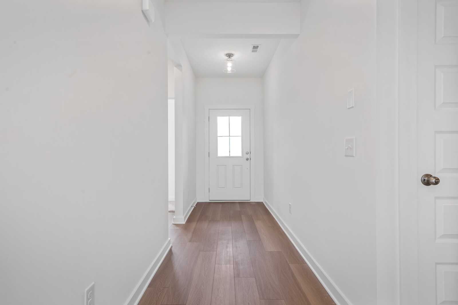 Bright hallway in The Asheville home design by Davidson Homes featuring white walls, hardwood floors, and front entry door