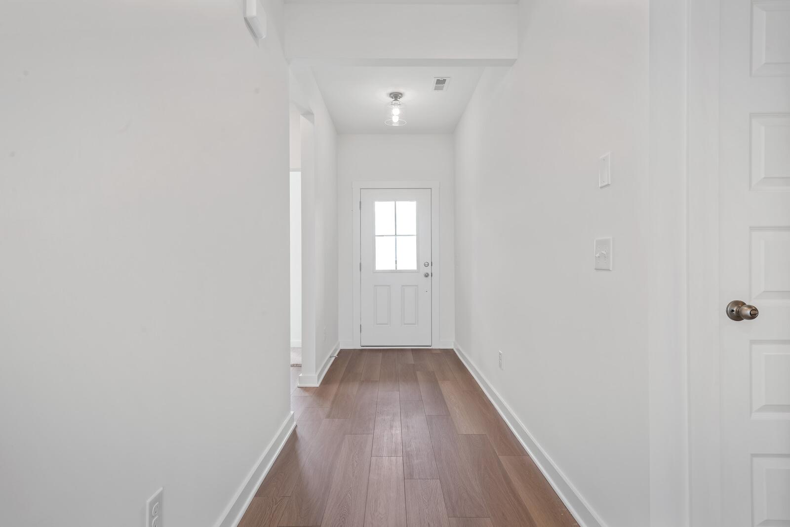 Spacious white hallway interior in The Asheville home with hardwood oak floors and glass-paneled entry door