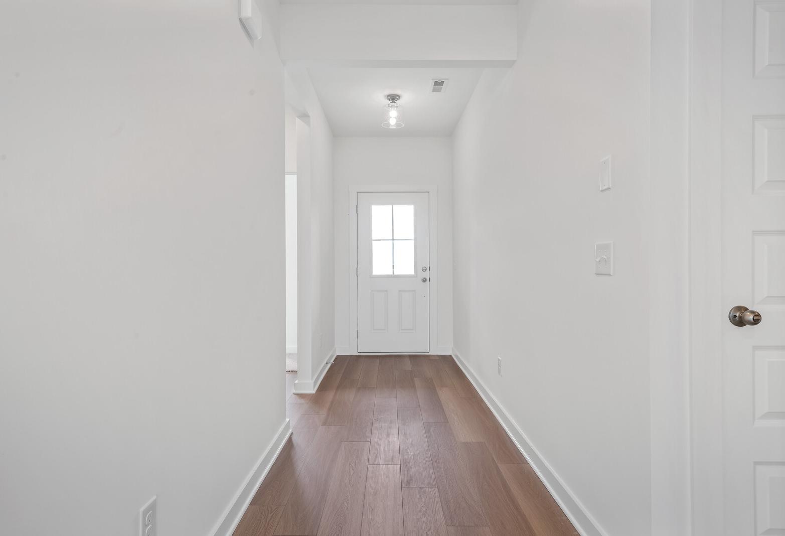 Spacious white hallway interior in The Asheville home with hardwood oak floors and glass-paneled entry door