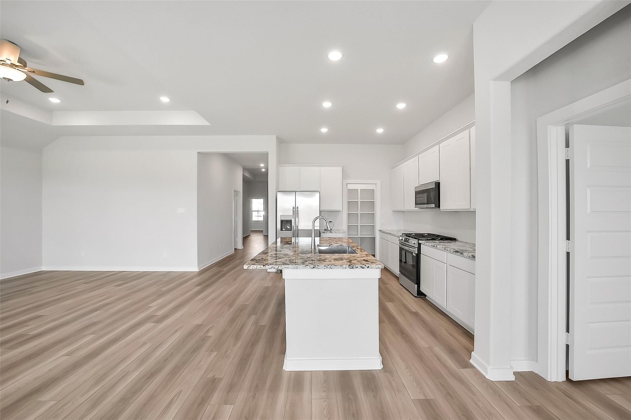 Modern open-concept kitchen with white cabinets, granite island, stainless appliances in The Acadia A by Davidson Homes, Katy, Texas