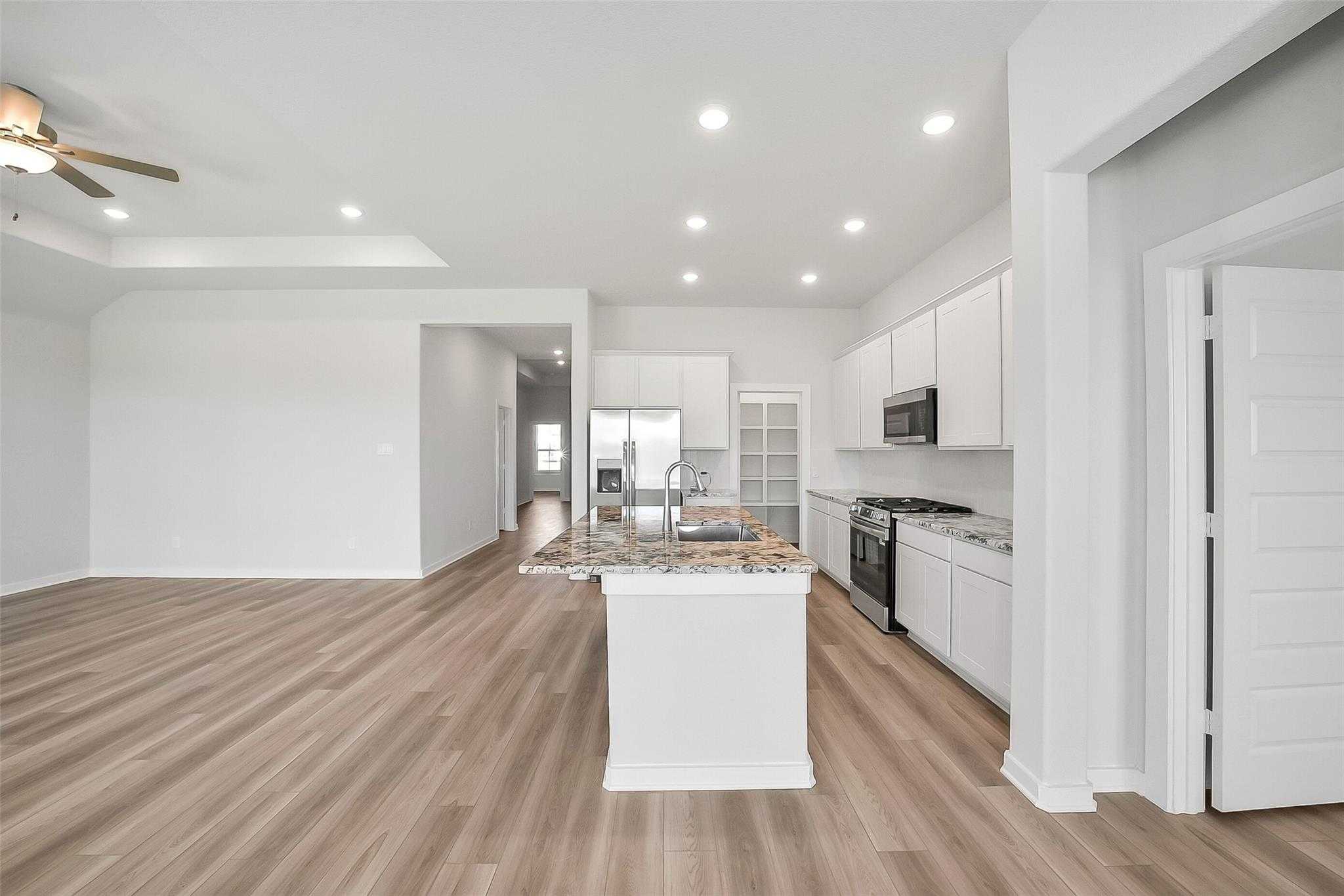 Modern open-concept kitchen with white cabinets, granite island, stainless appliances in The Acadia A by Davidson Homes, Katy, Texas