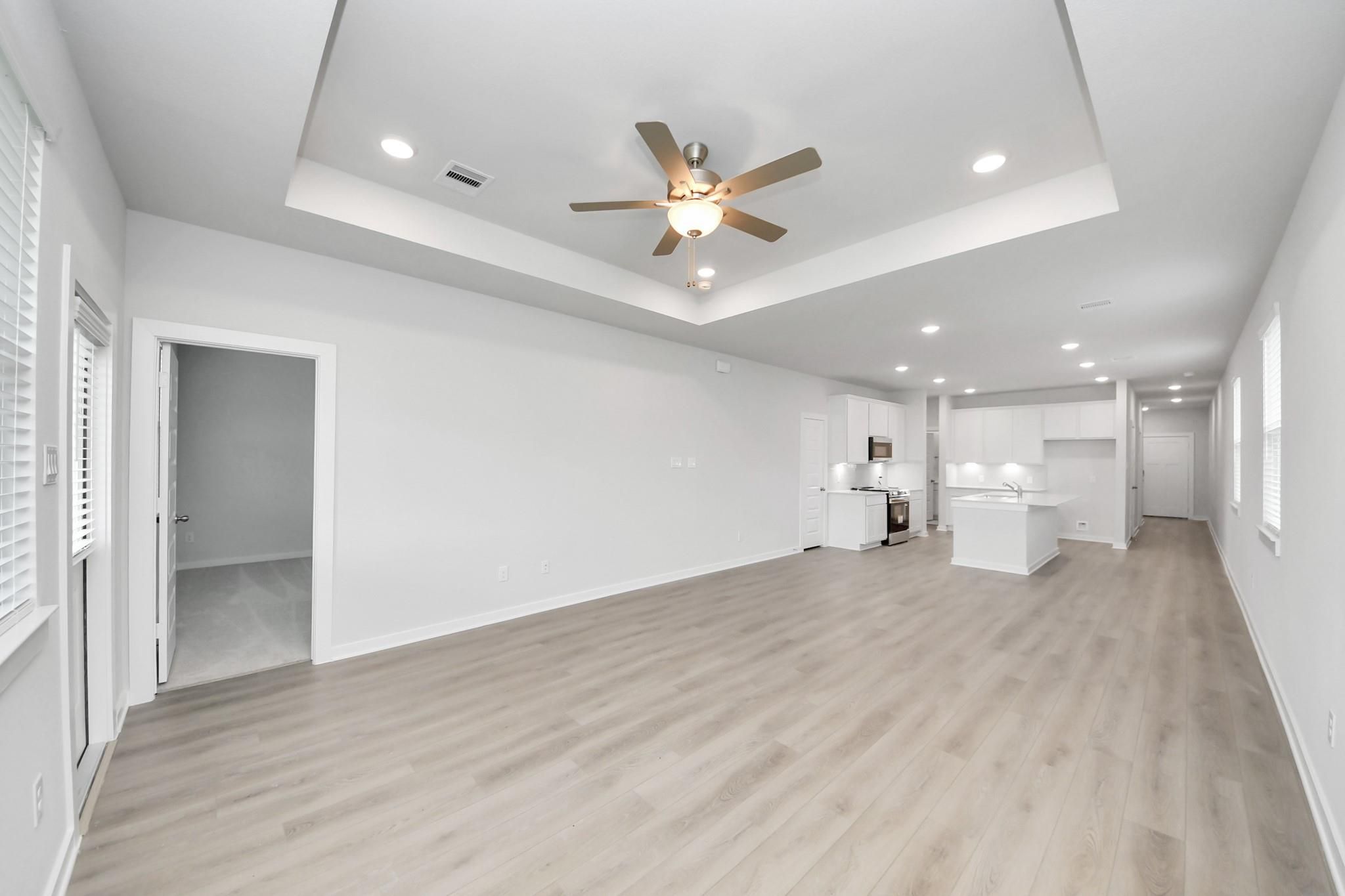 Open-concept living room and modern kitchen with tray ceiling in The Frio F floor plan at Liberty Estates, Cleveland, TX.