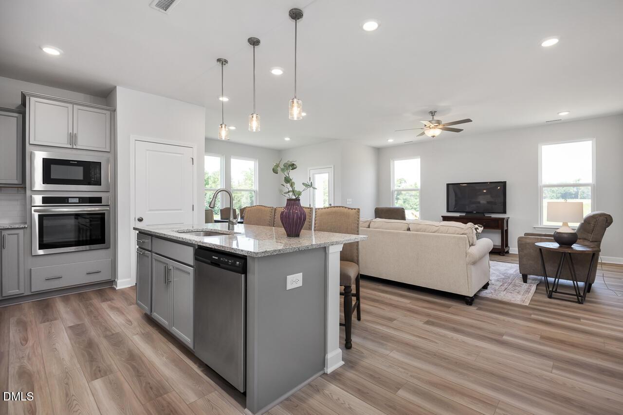 Modern open-concept kitchen with stainless appliances, granite island, white cabinets, and cozy living room in Davidson Homes The Daphne D, Zebulon, NC