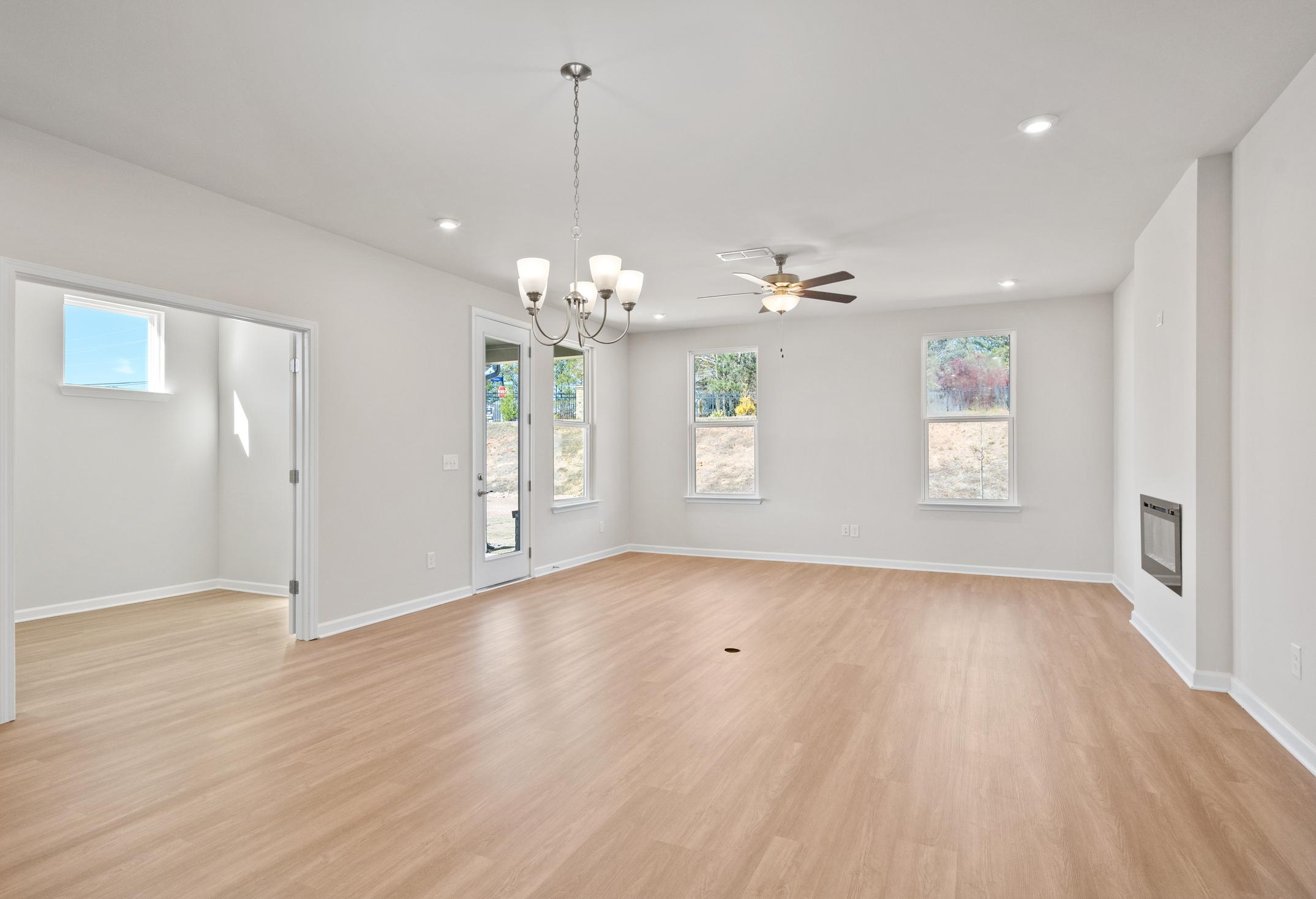 Spacious open-concept living room in The Dawson C with hardwood floors, fireplace, chandelier, and large windows
