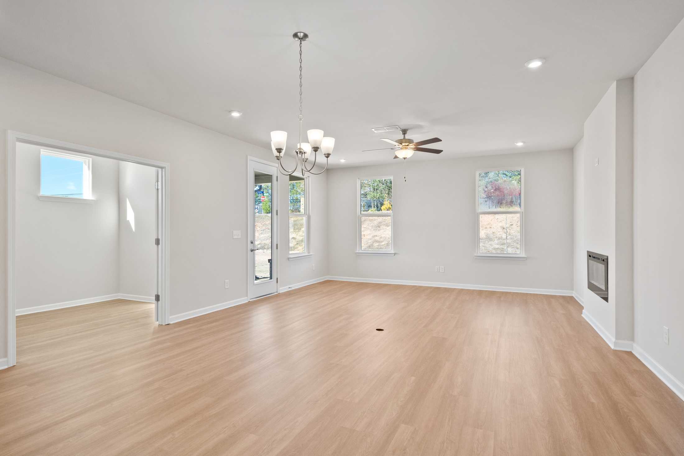Spacious open-concept living room in The Dawson C with hardwood floors, fireplace, chandelier, and large windows