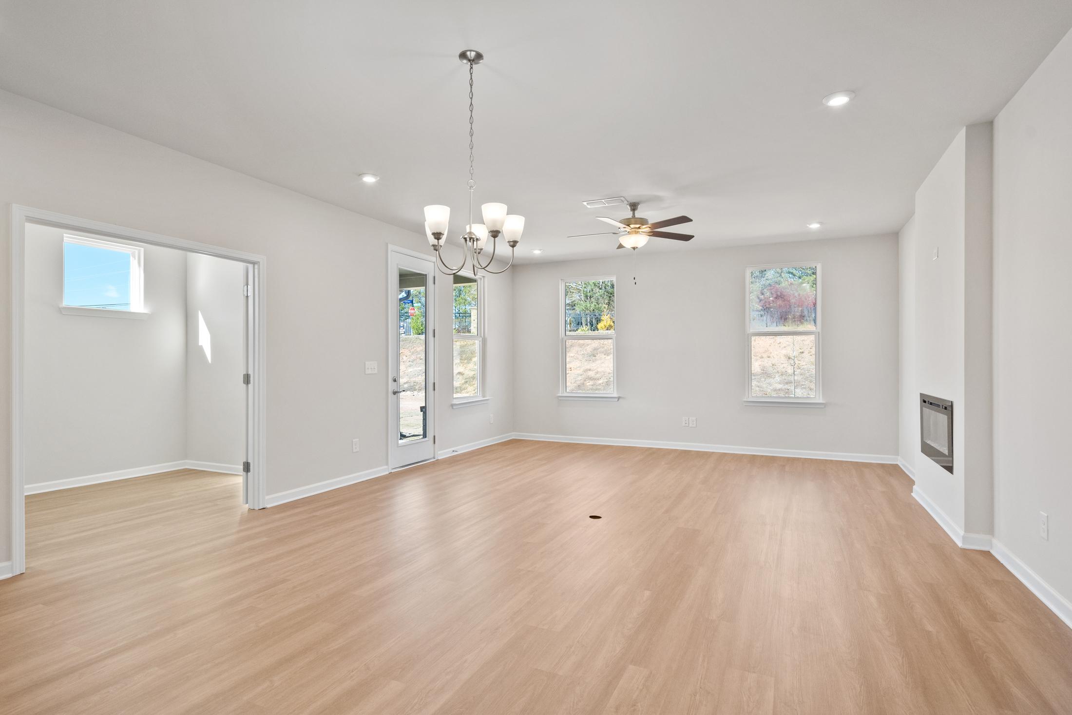 Spacious open-concept living room in The Dawson C with hardwood floors, fireplace, chandelier, and large windows
