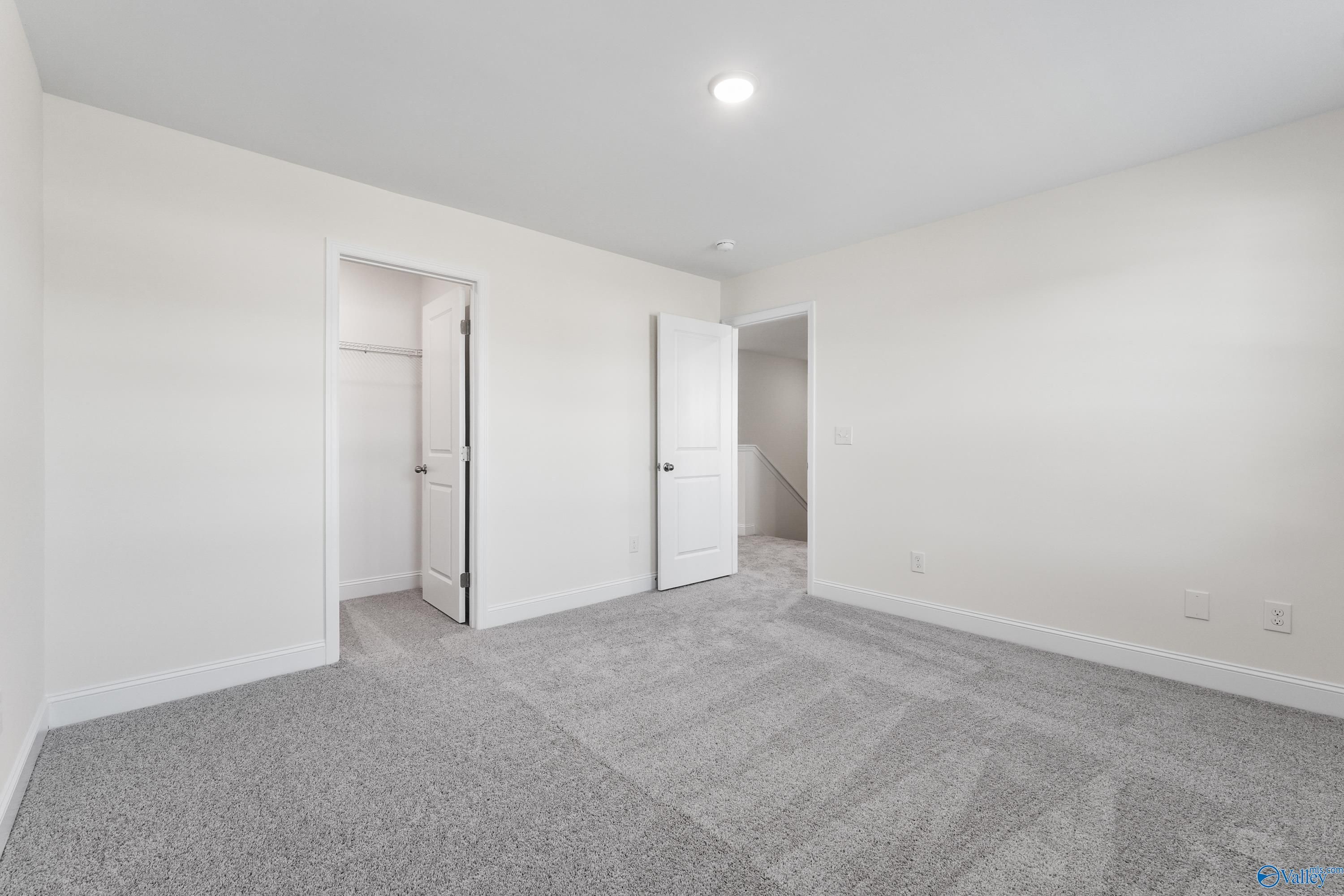 Spacious bedroom with louvered walk-in closet, gray carpet, and white walls in Davidson Homes The Shelby A, Athens, Alabama
