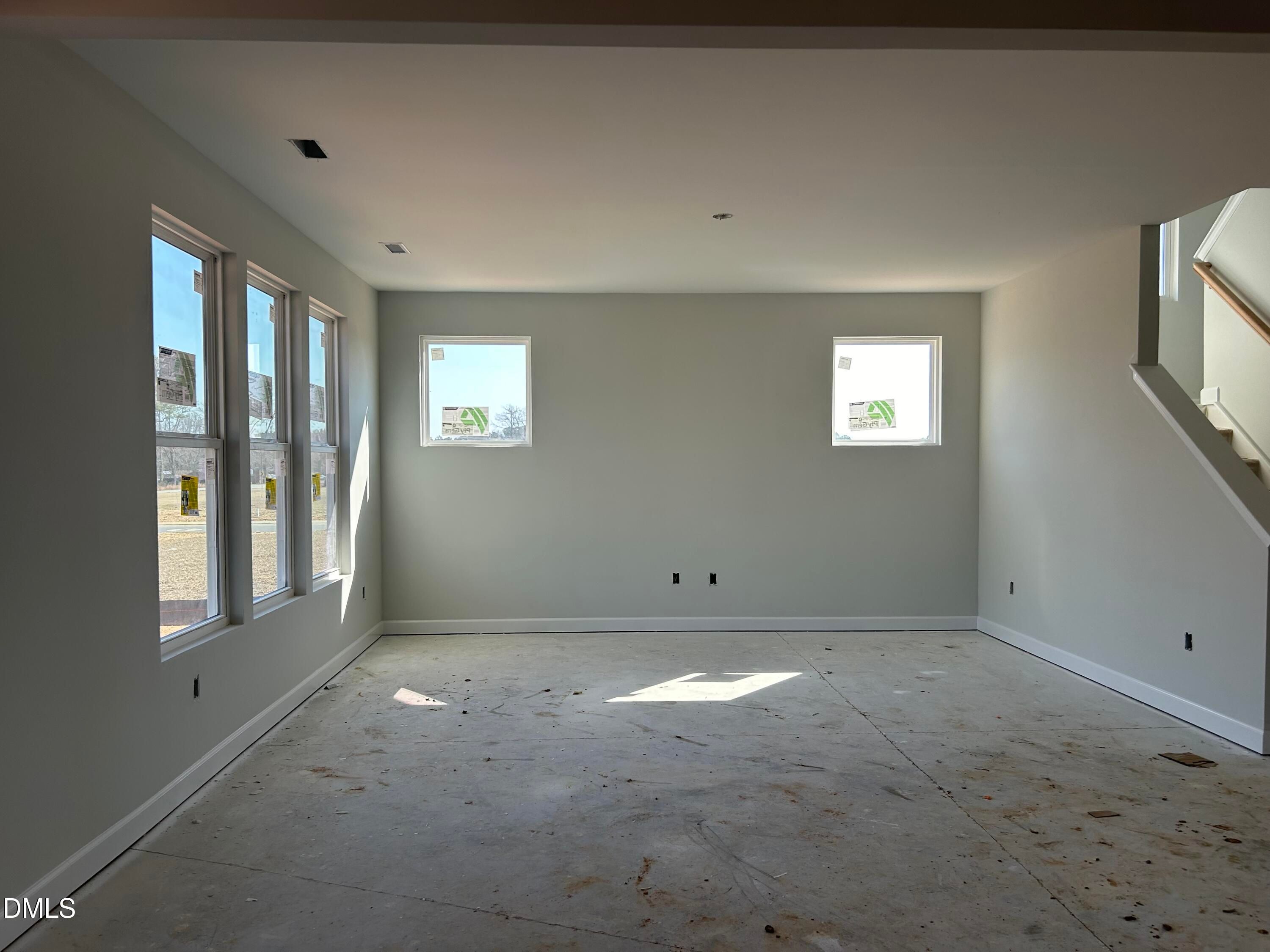 Bright unfinished great room with large windows, natural light, and staircase in The Chestnut B home, Lillington, NC
