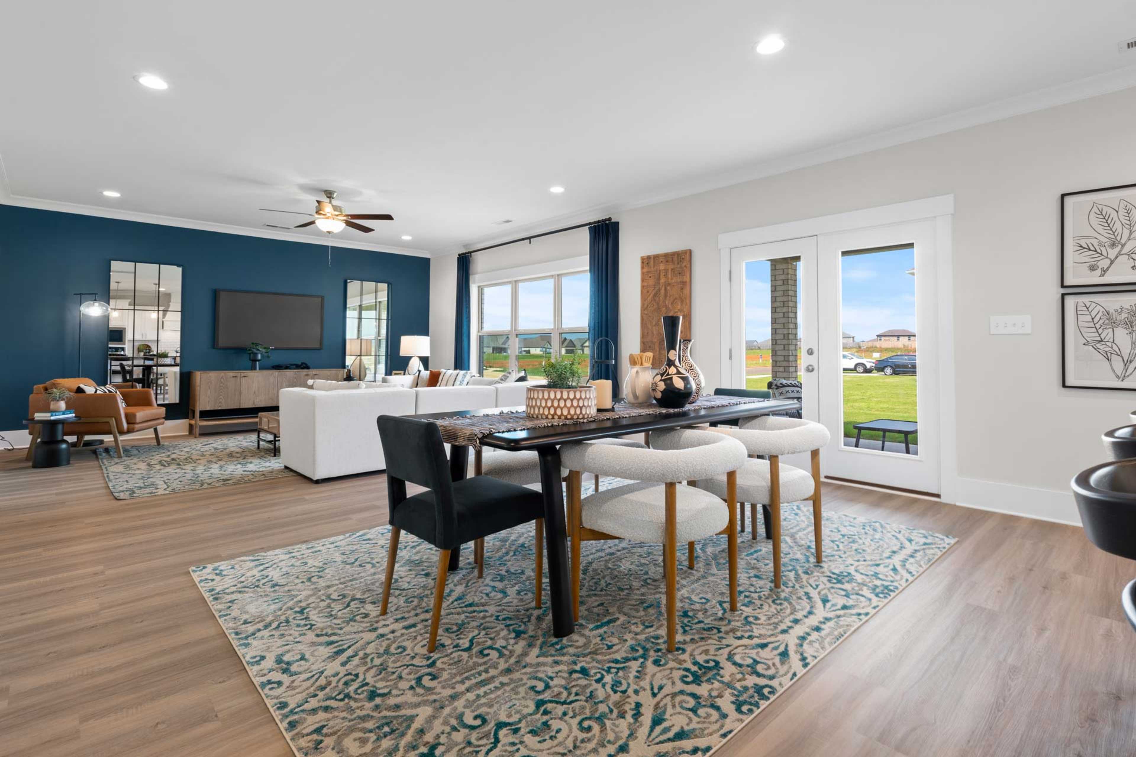 Spacious open-concept living and dining area at Walker's Hill in Meridianville AL with navy accent wall, hardwood floors, and large windows to backyard