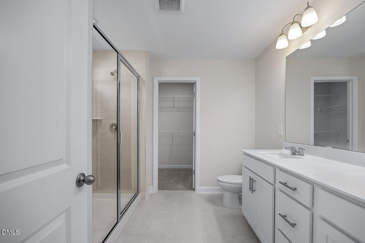 Modern master bathroom with frameless glass shower, white double vanity, and walk-in closet in Davidson Homes The Grace C, Lillington, NC