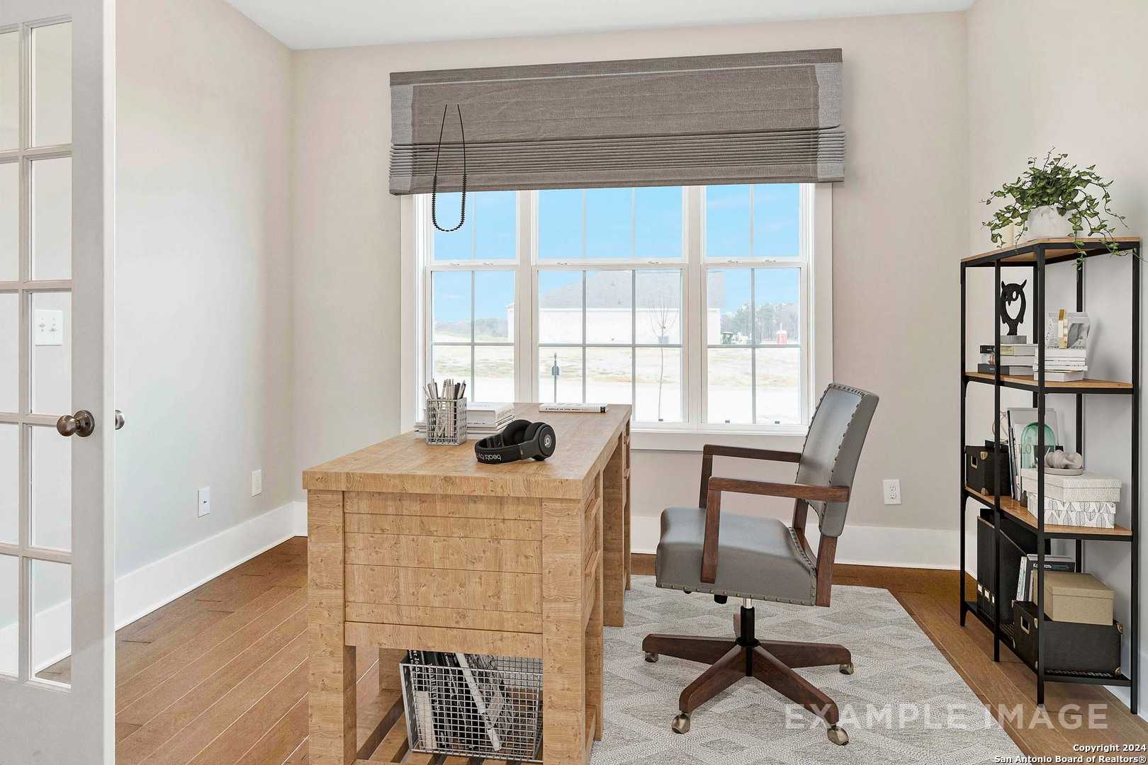 Bright home office with oak desk, gray swivel chair, metal bookshelf, and large window in Davidson Homes The Lanier H, Ladera, San Antonio