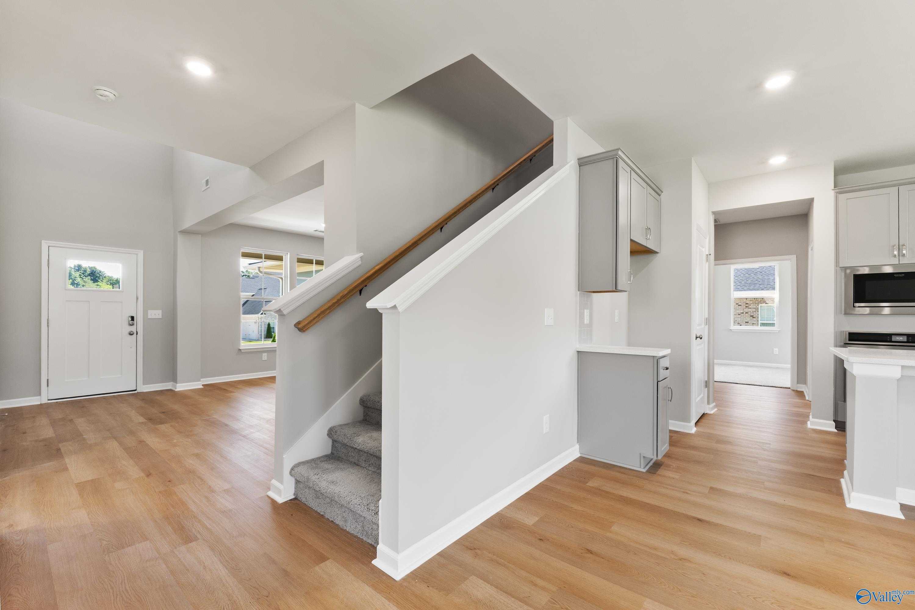 Open foyer with hardwood floors, wooden staircase, and modern kitchen in 2-story The Charm home, Riverton Preserve, Huntsville, Alabama