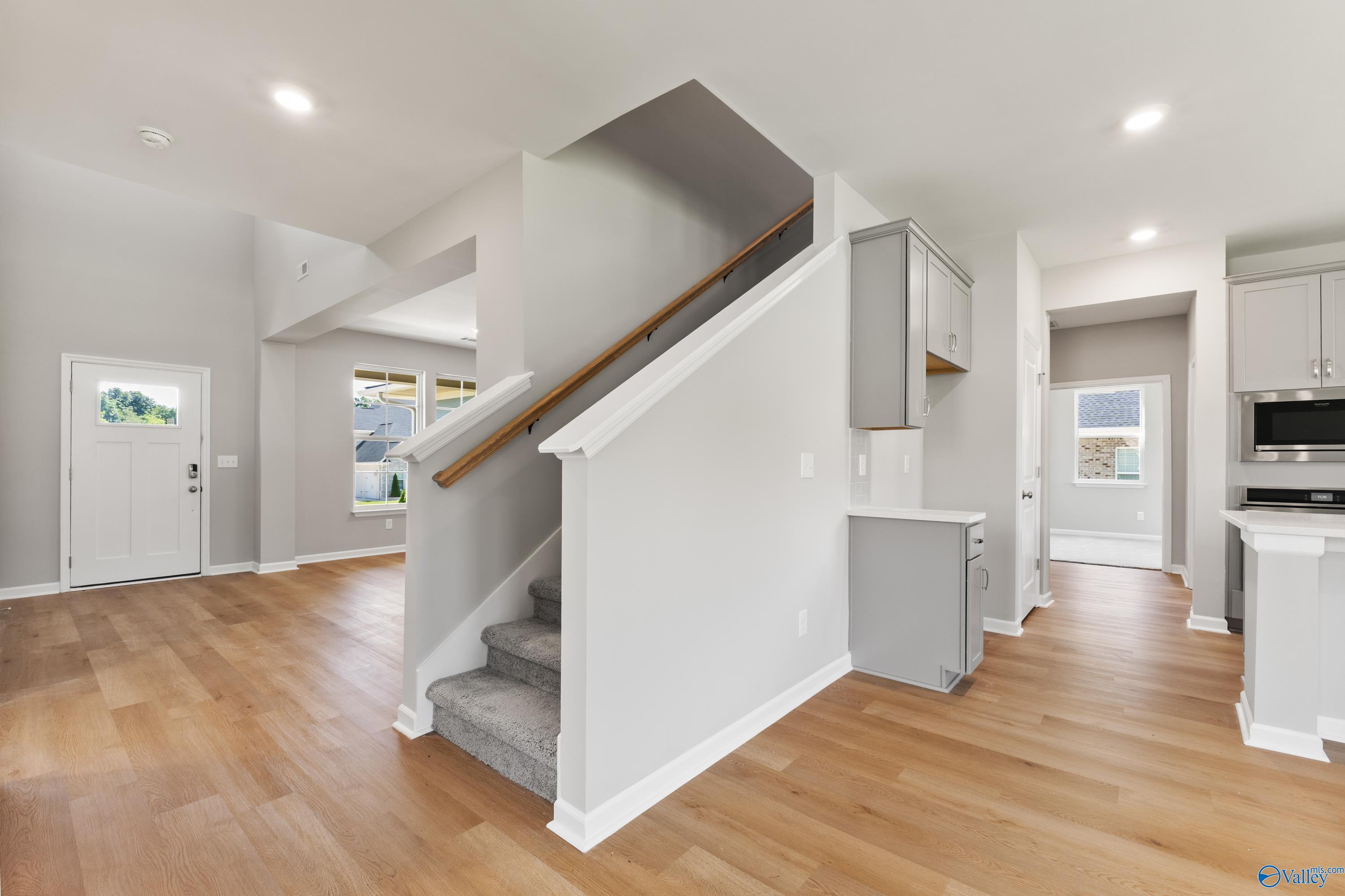 Bright open entryway with hardwood floors, white staircase, and modern kitchen in Davidson Homes The Charm, Huntsville AL