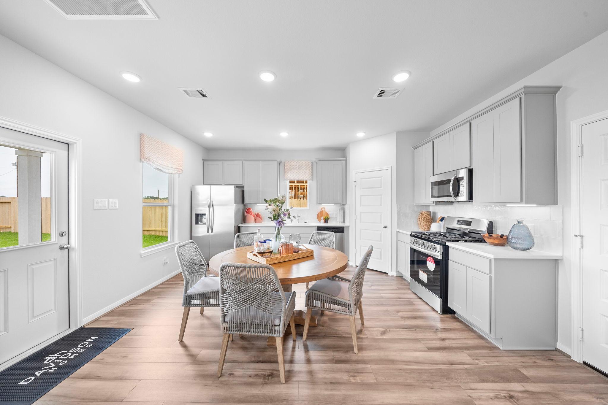 Spacious open-concept kitchen and dining at Hill & Dale Ranch in Splendora TX with white cabinets, round wood table, and hardwood floors