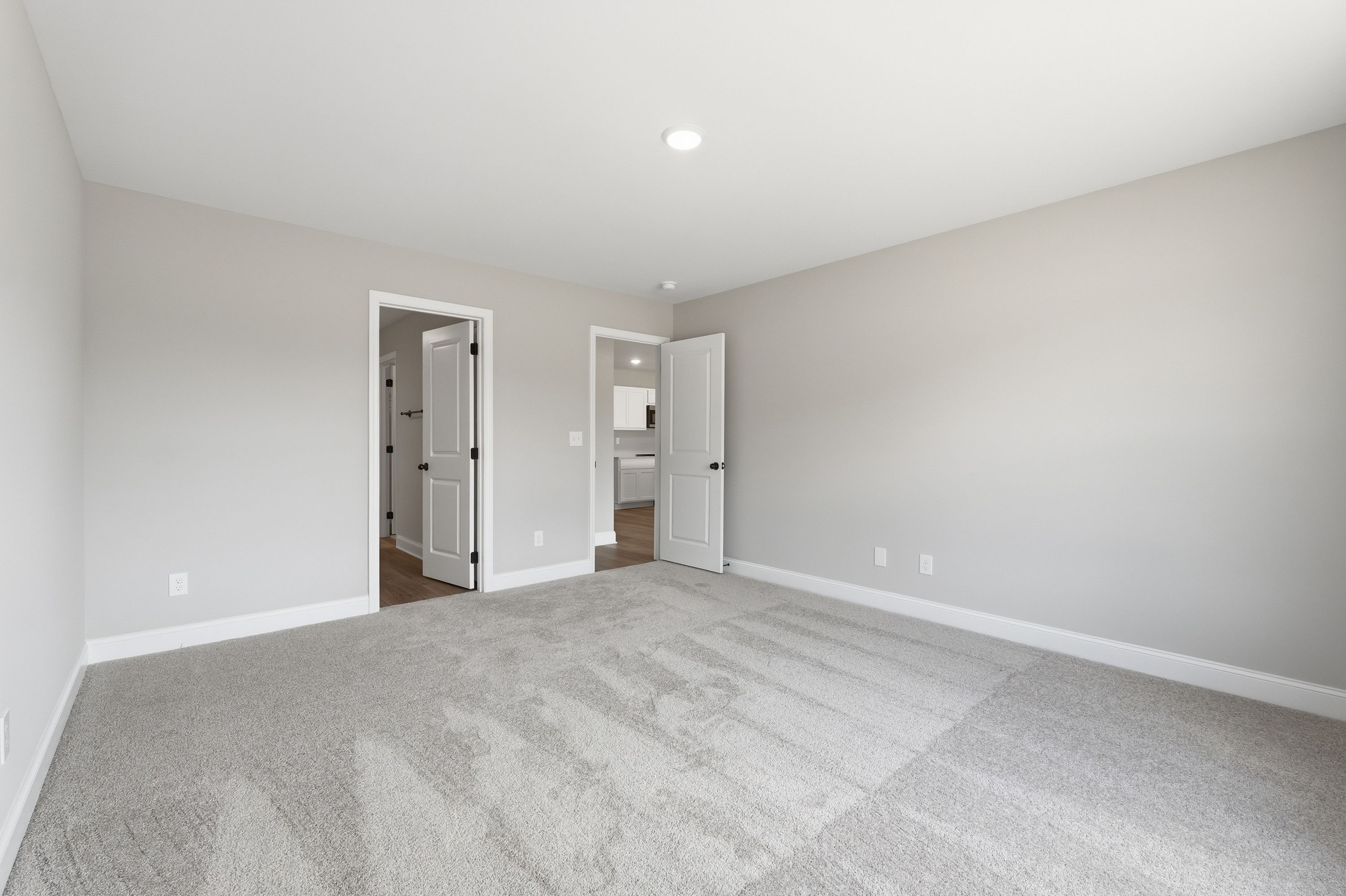 Spacious master bedroom in The Daphne V with light gray walls, plush carpet, en-suite bath door, and closet access