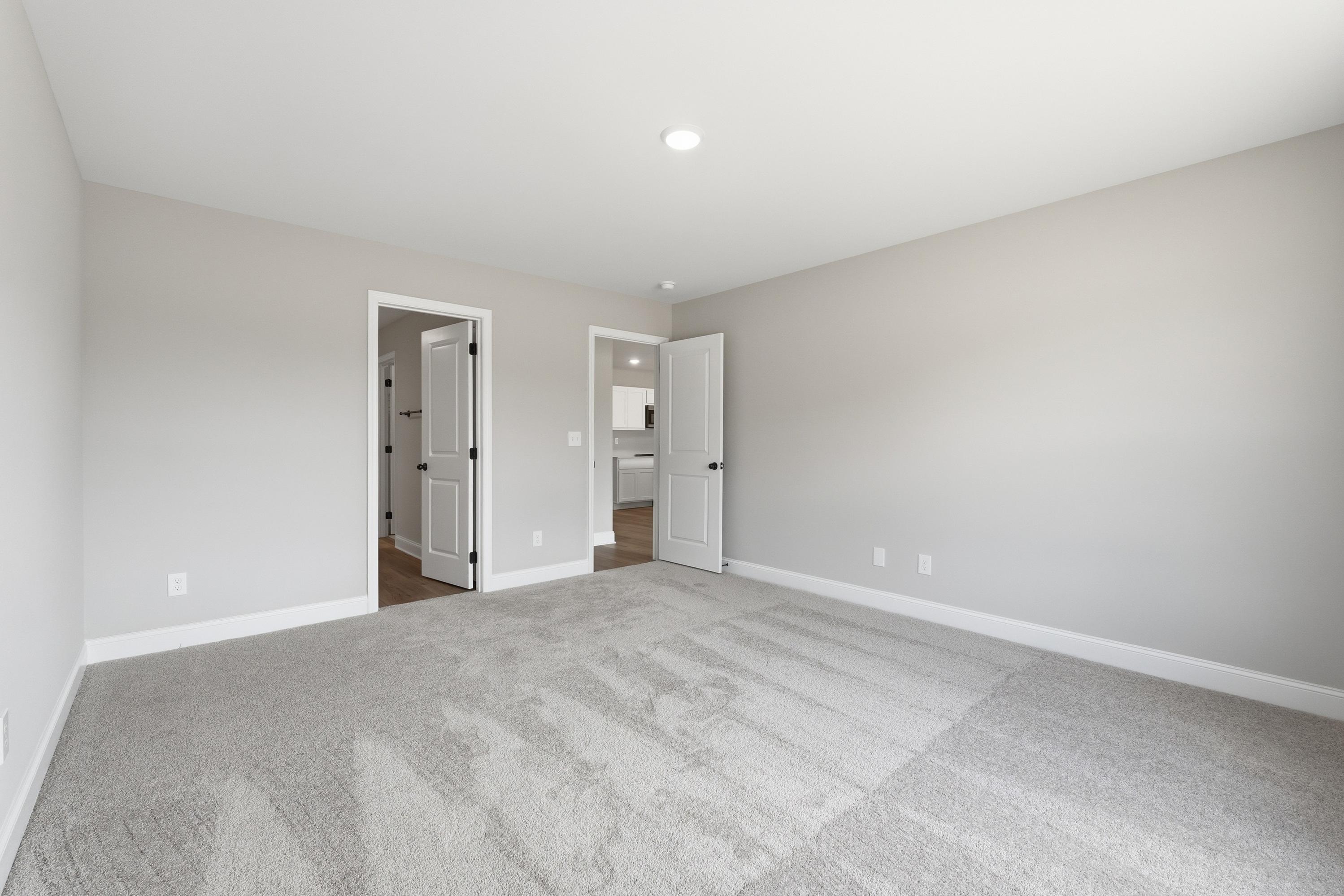 Spacious master bedroom in The Daphne V with light gray walls, plush carpet, en-suite bath door, and closet access
