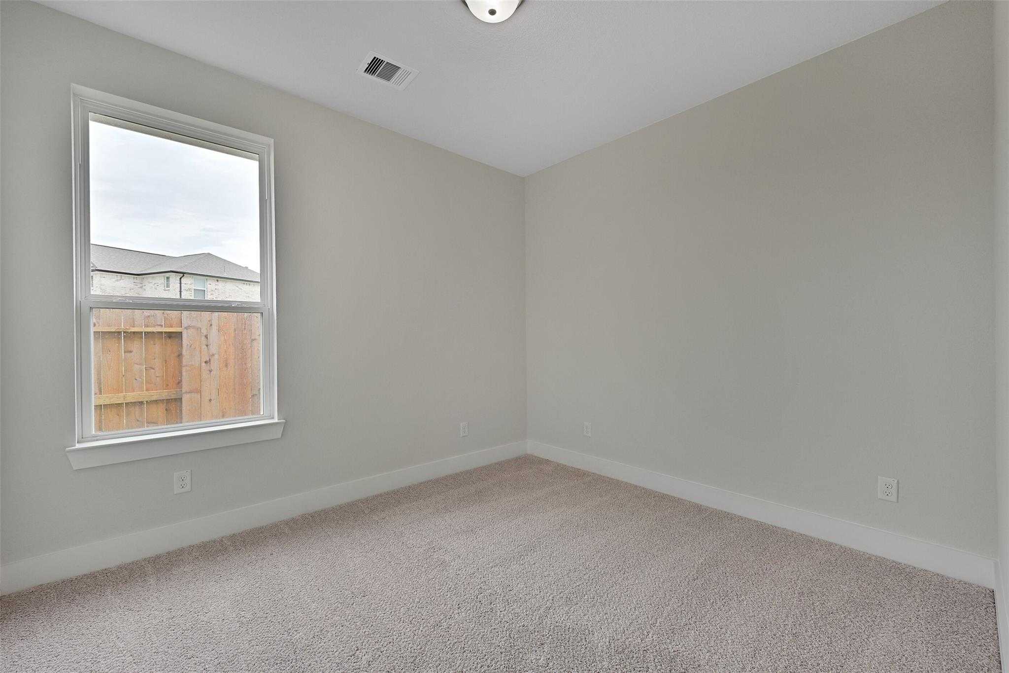 Bright secondary bedroom with light gray walls, large window to fenced yard, and carpet in Davidson Homes The Edward C, Lago Mar, Texas City