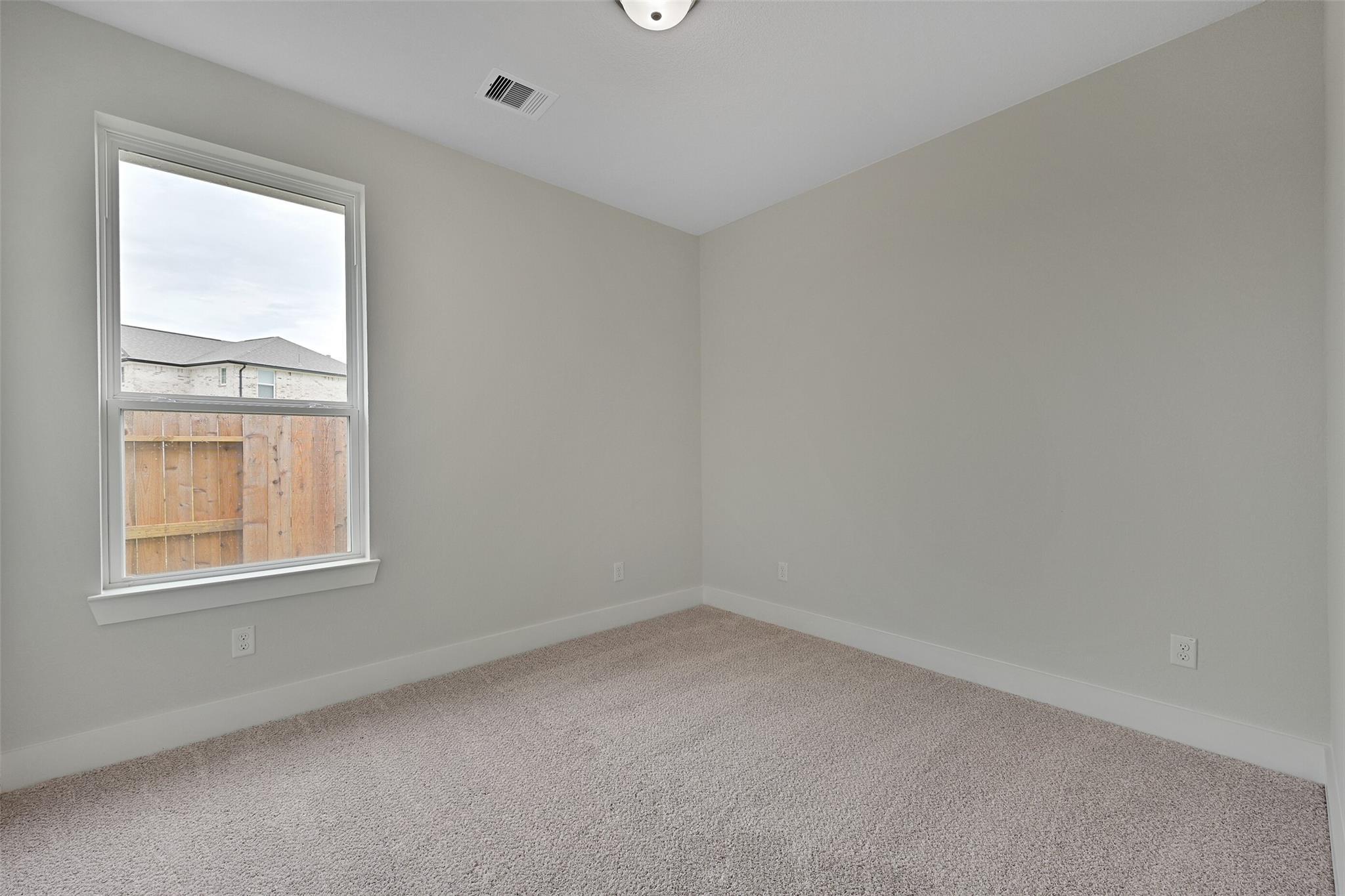 Cozy secondary bedroom with light gray walls, plush carpet, large window overlooking fenced backyard in Davidson Homes The Edward C, Texas City