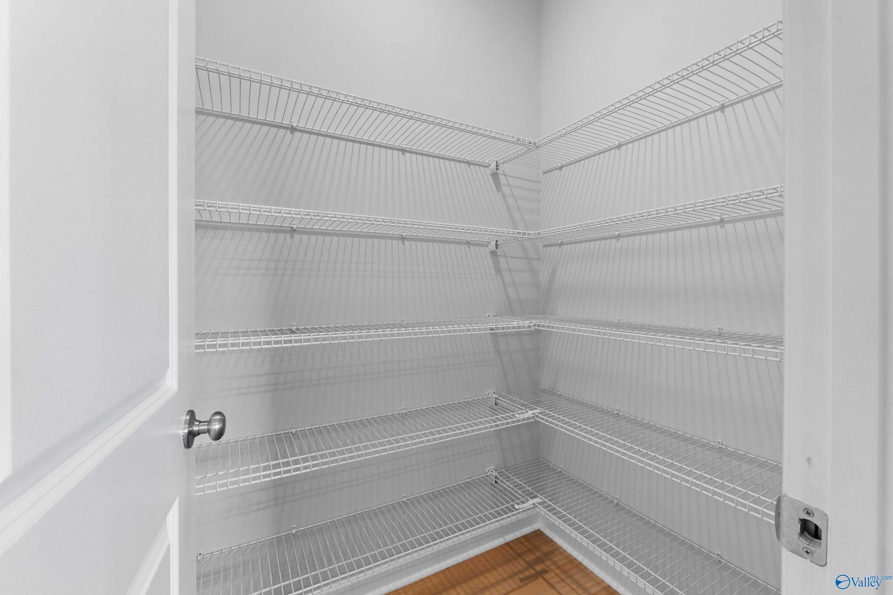 Empty walk-in closet with white wire shelving, open door, and hardwood floor in The Aurora 4-bedroom home, Evermore Homes, Harvest AL