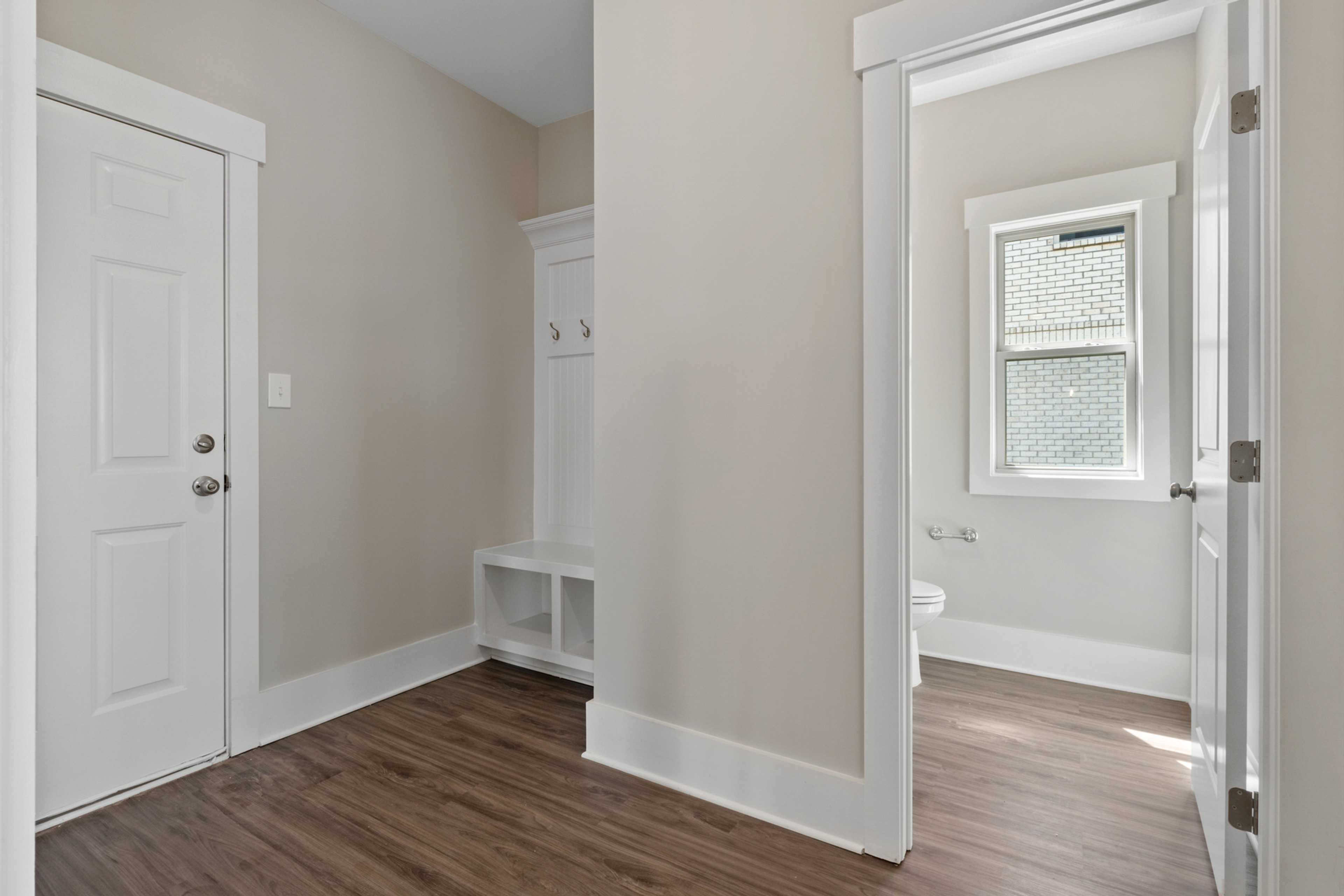 Mudroom with built-in bench, coat hooks, and hardwood floors at Little Burwell Estates in Harvest AL adjacent to powder room