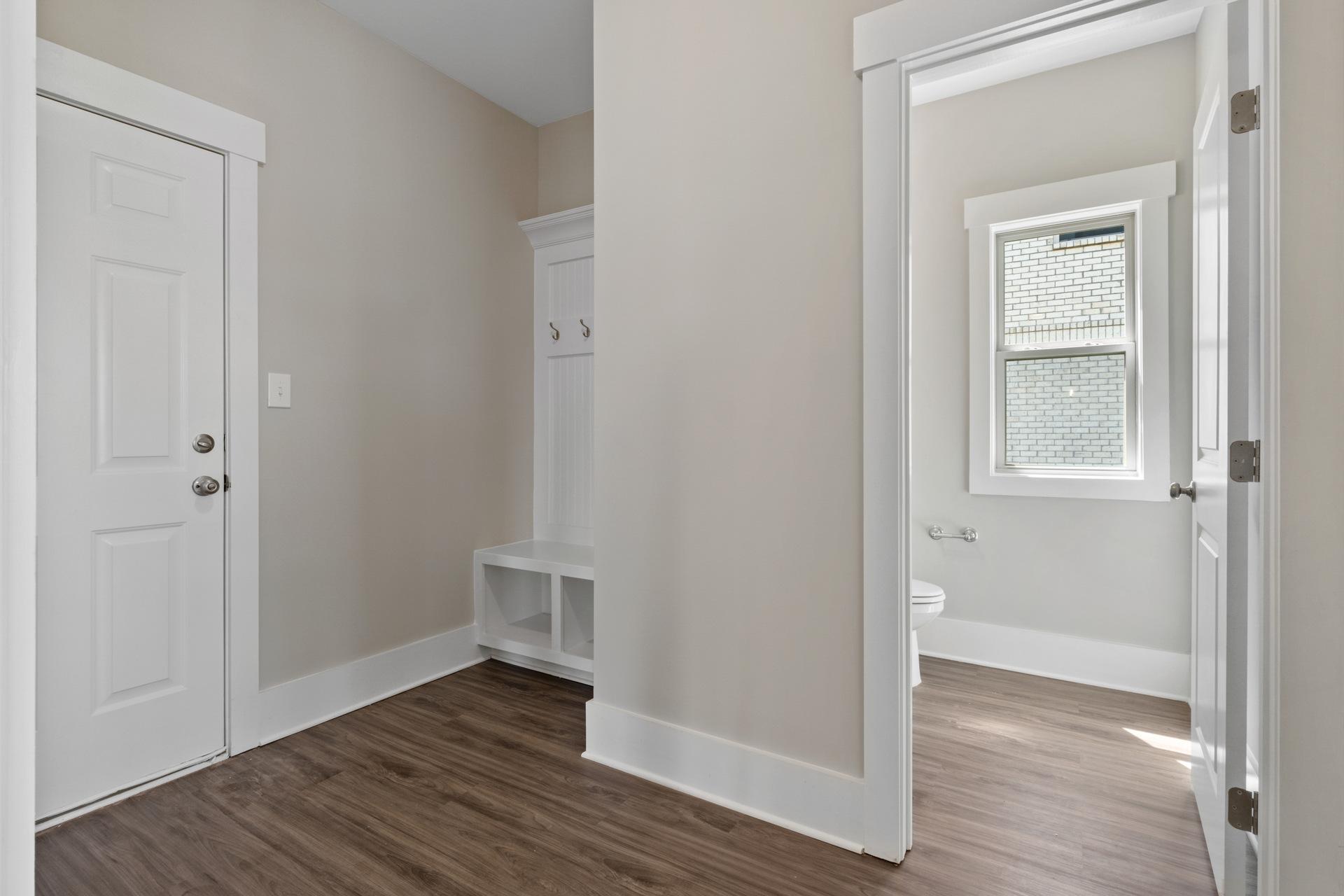 Mudroom with built-in bench, coat hooks, and hardwood floors at Little Burwell Estates in Harvest AL adjacent to powder room